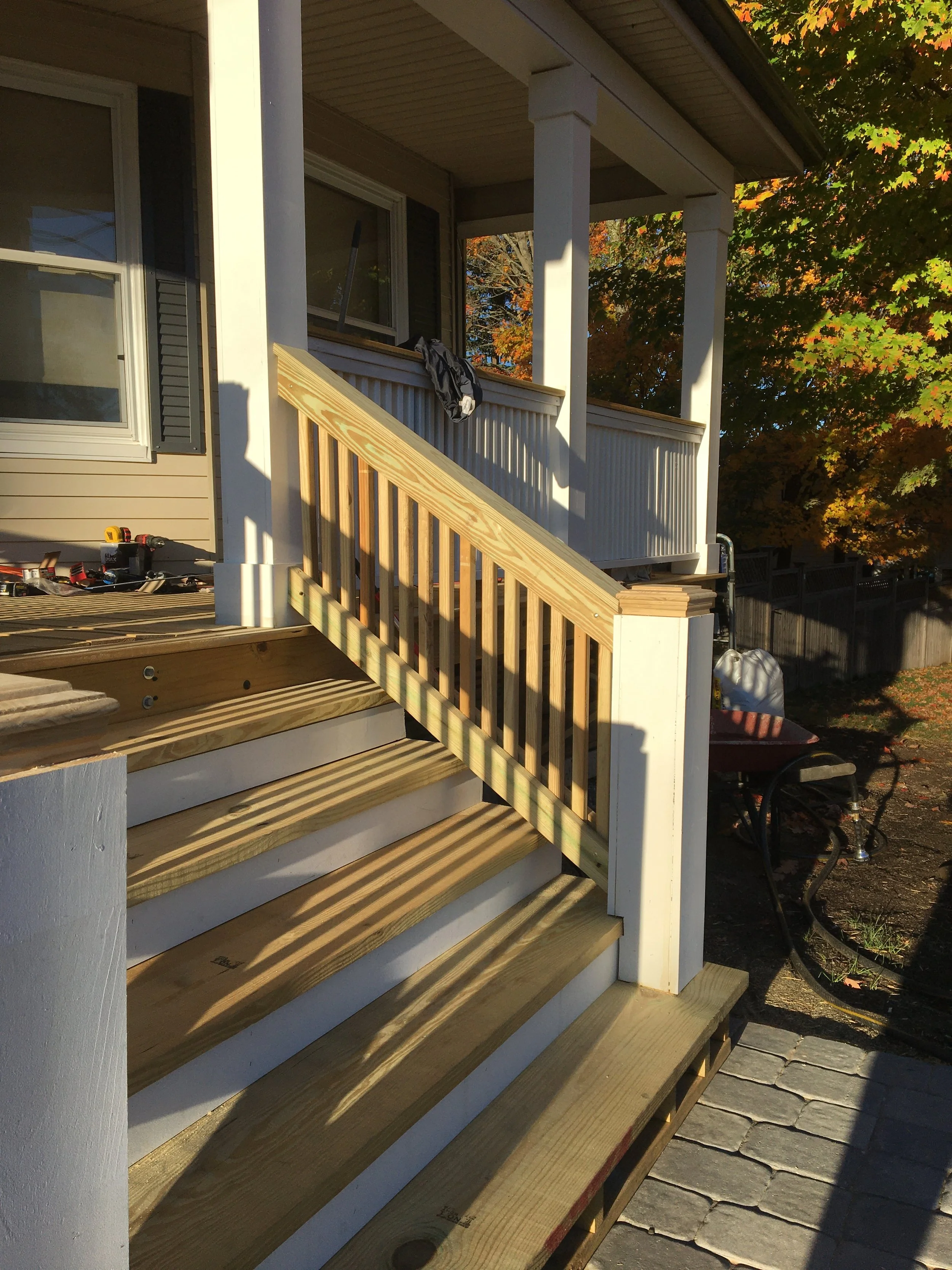Construction of a new wooden staircase and railing on a house porch during daytime.