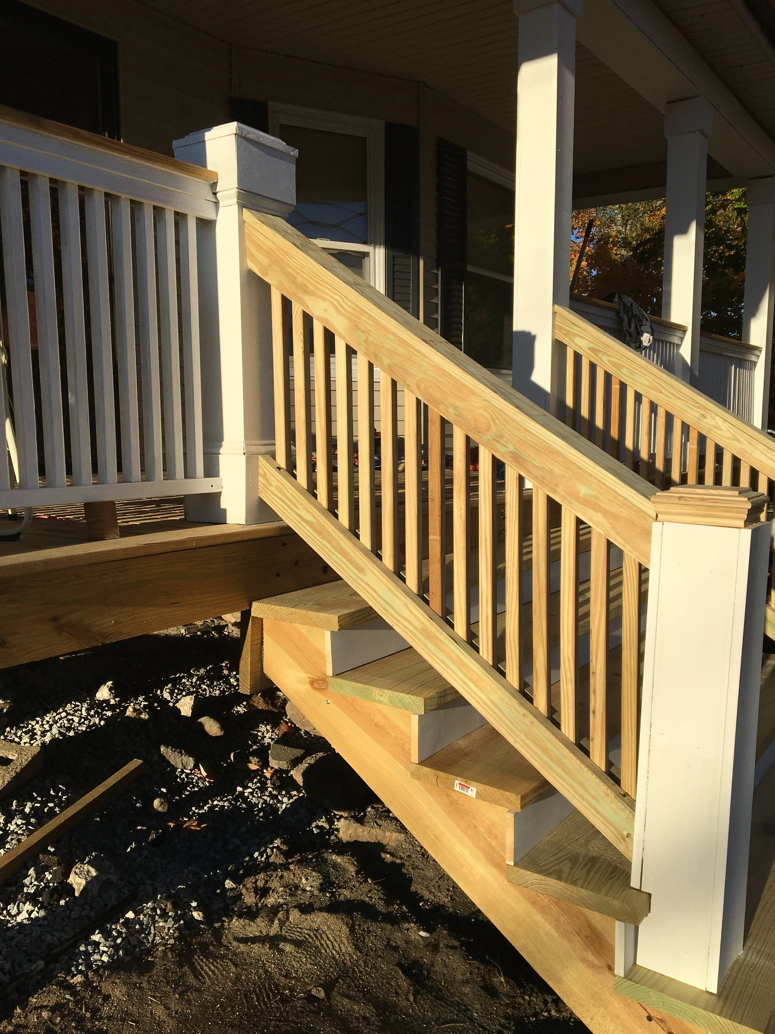 Wooden staircase under construction on a porch, with a white railing and posts.