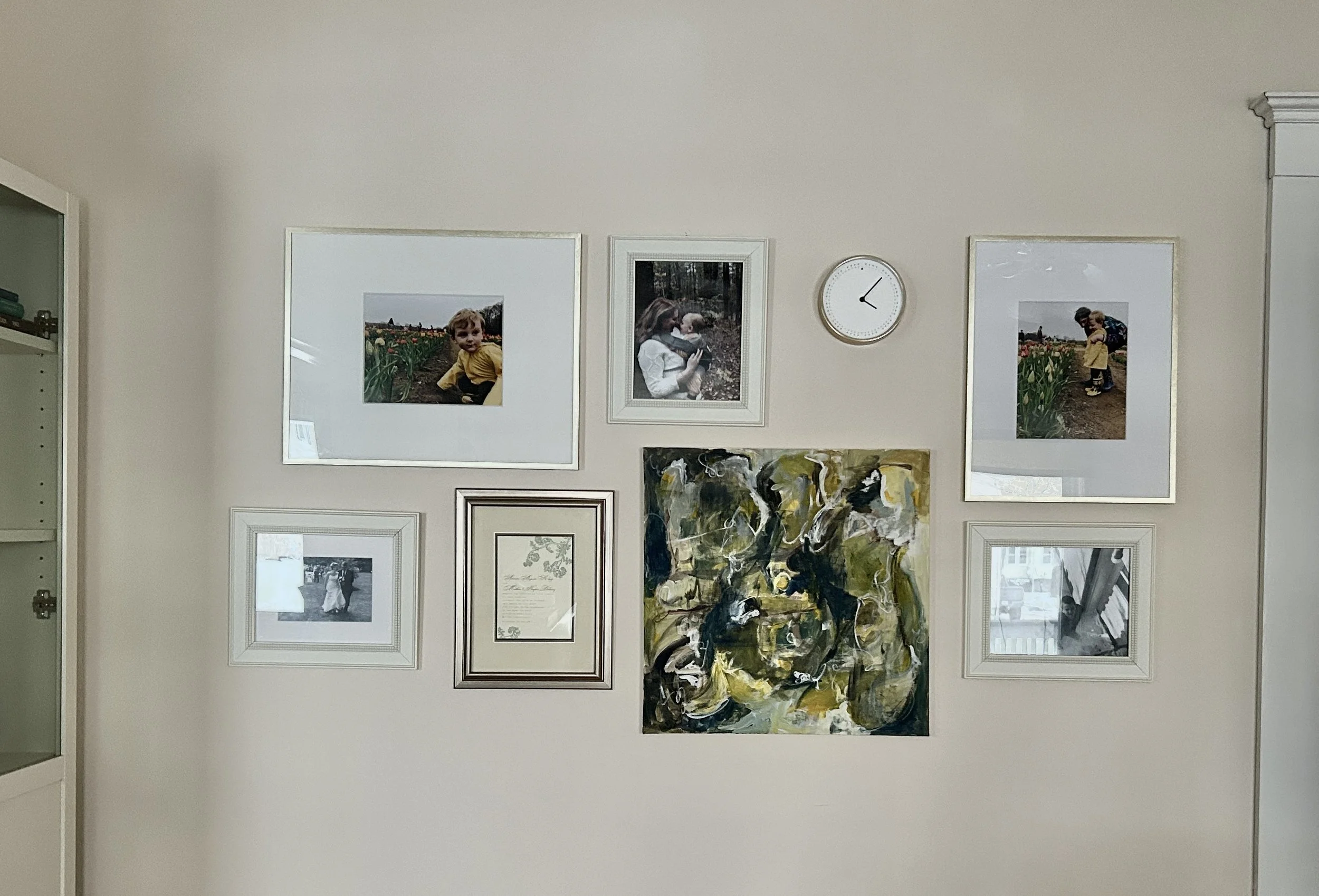 A wall decorated with a collection of framed photographs, paintings, and a clock, including images of children, a person with a dog, and abstract artwork.