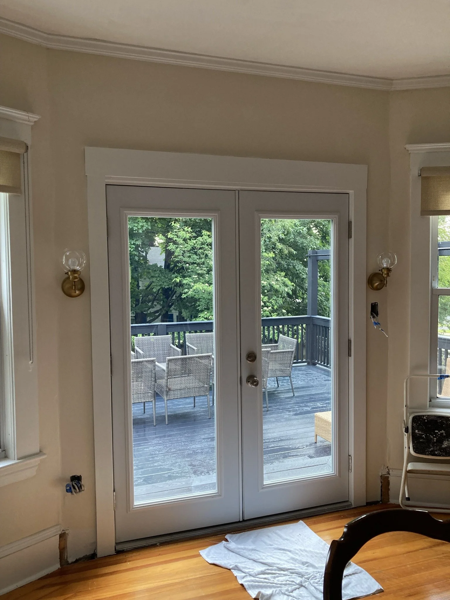 Interior view of a room with glass double doors leading to a wooden deck with outdoor chairs, and green trees outside.