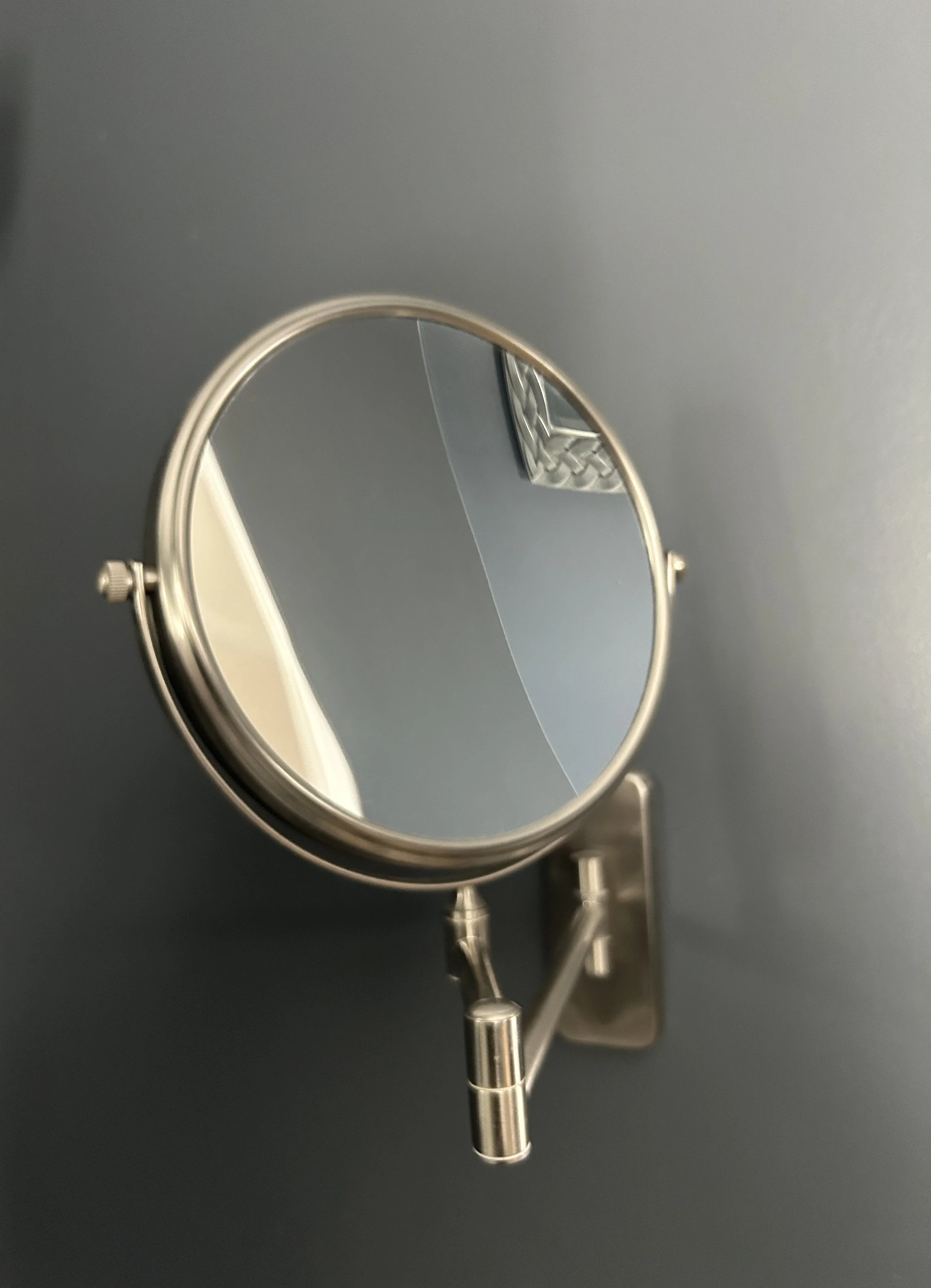 A small round mirror attached to a wall with a metal arm.