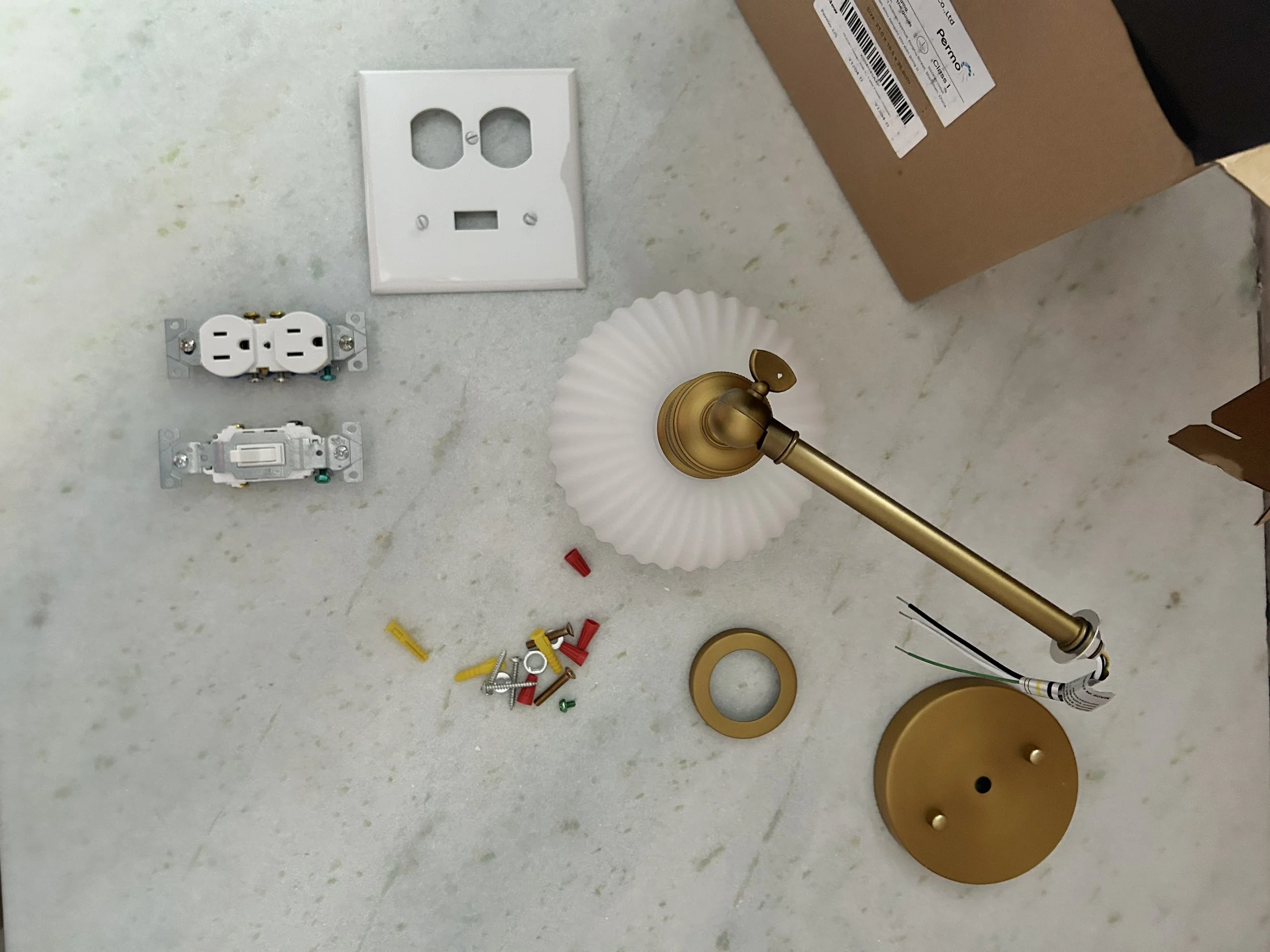Disassembled brass and white wall lamp with electrical components, wiring, screws, and mounting hardware on a white surface.