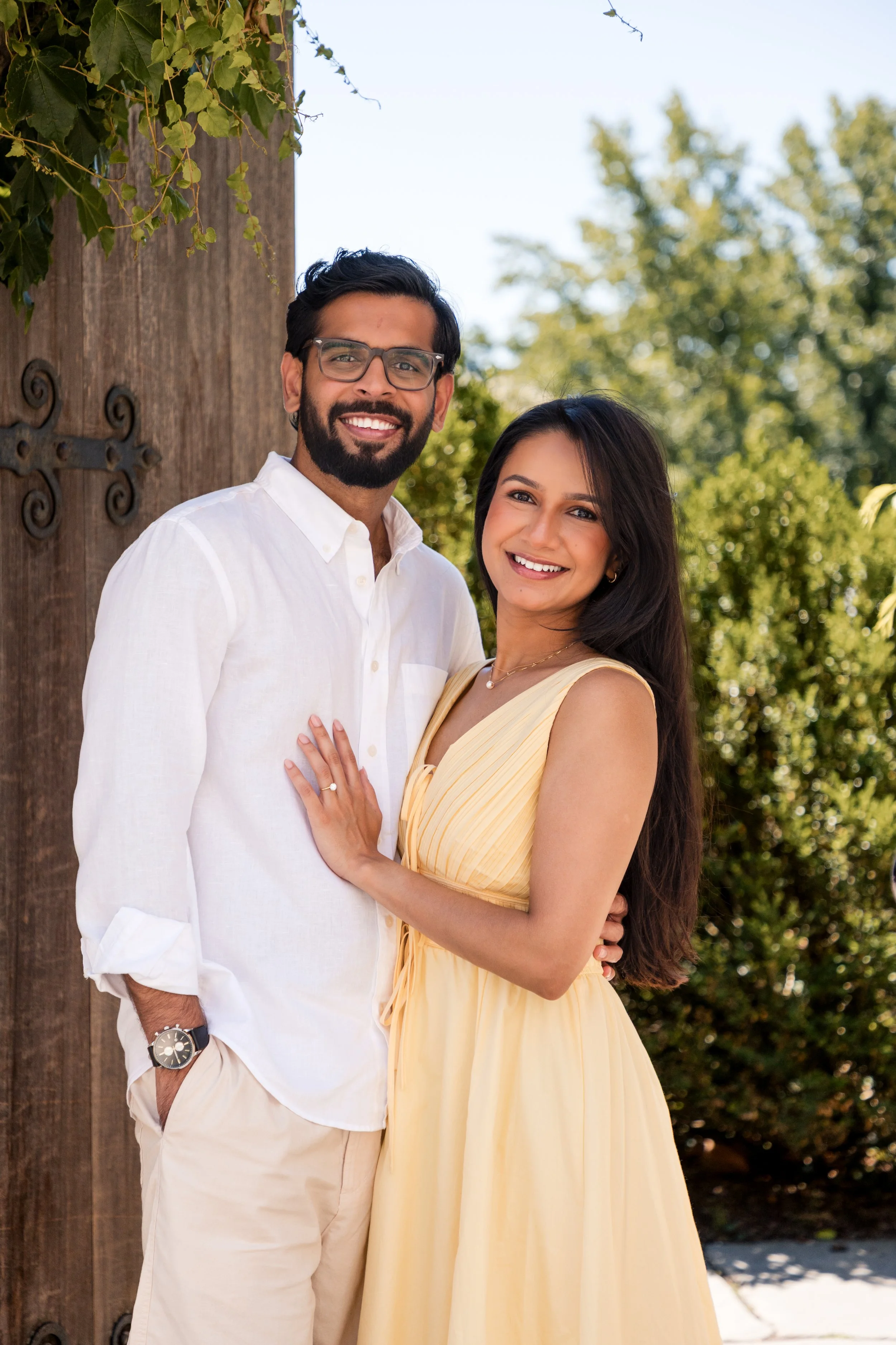 Engaged couple in white and yellow smiling together in a sunlit garden