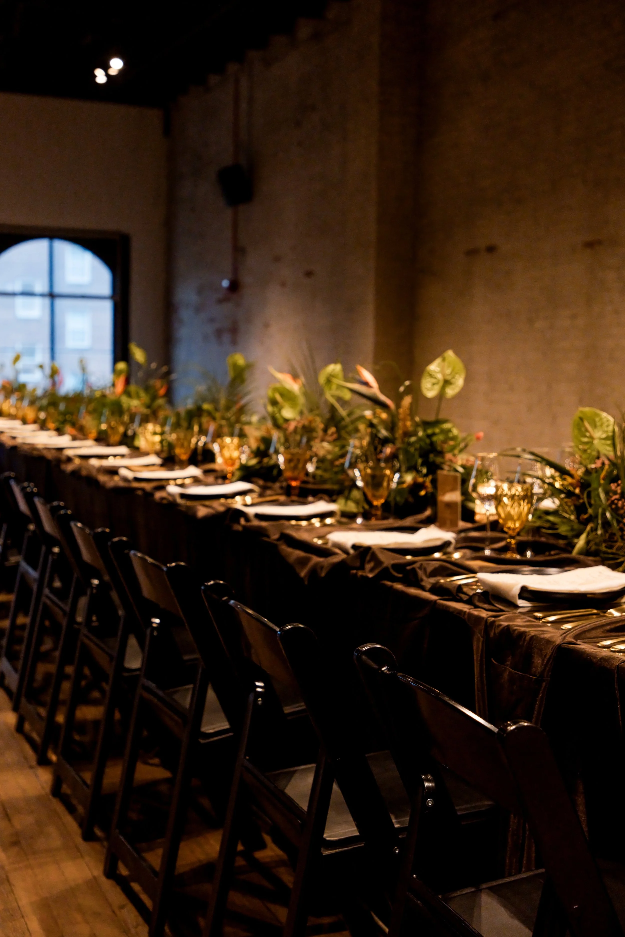 Guests seated along a greenery-lined dinner table in a warmly lit venue, Baltimore event photography