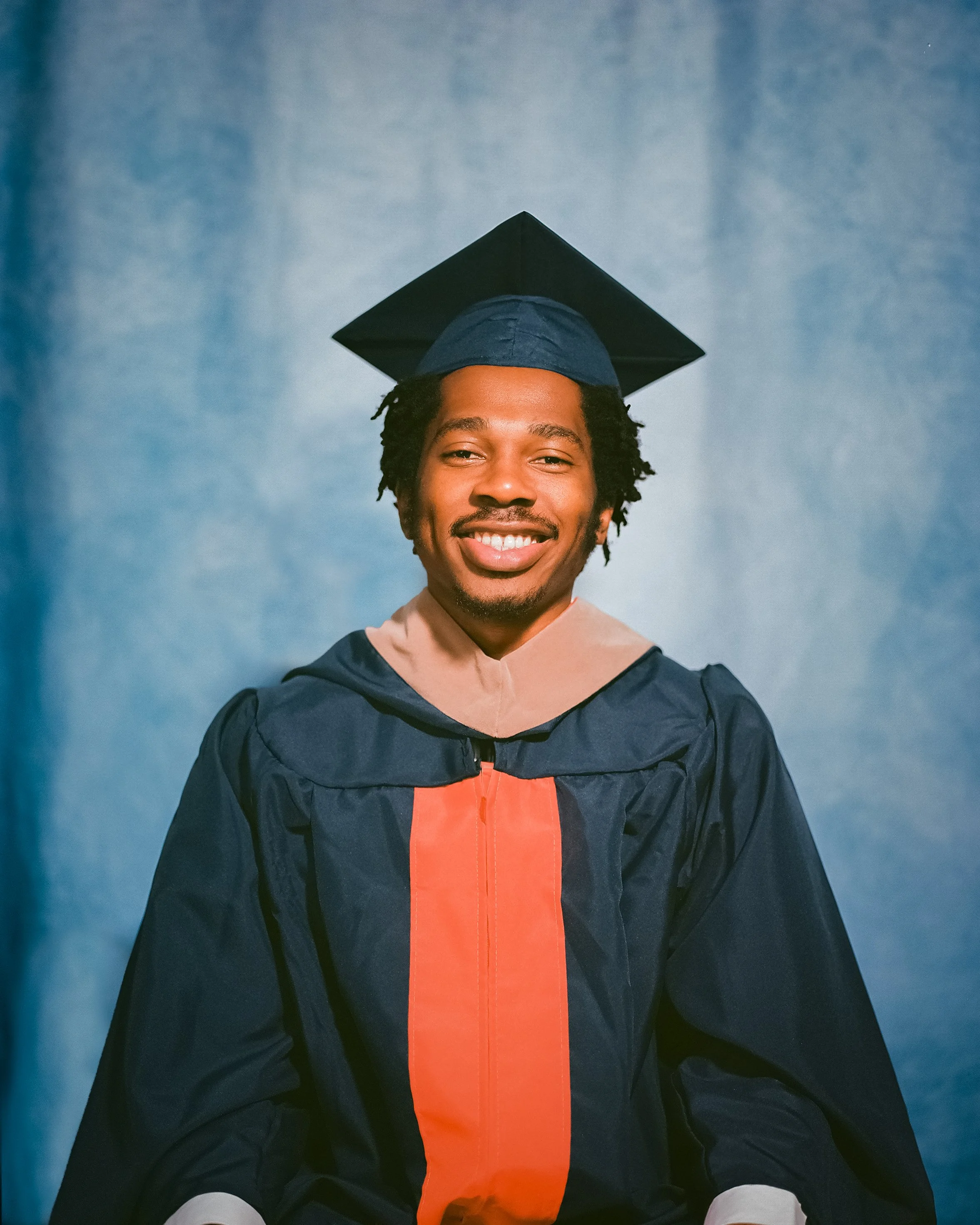 A young man dressed in a graduation gown and cap, smiling at the camera.
