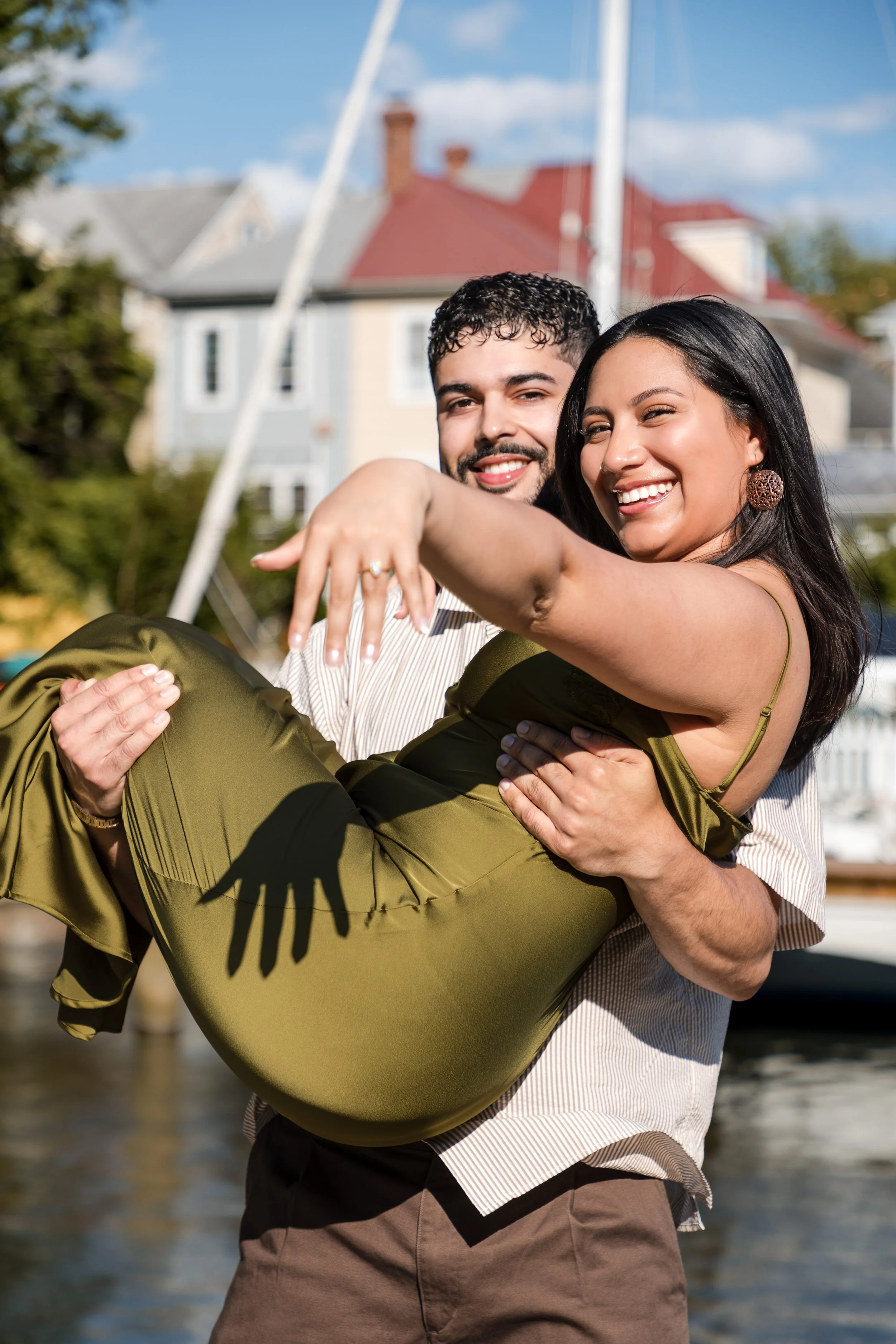 Newly engaged couple laughing as he lifts her by the waterfront