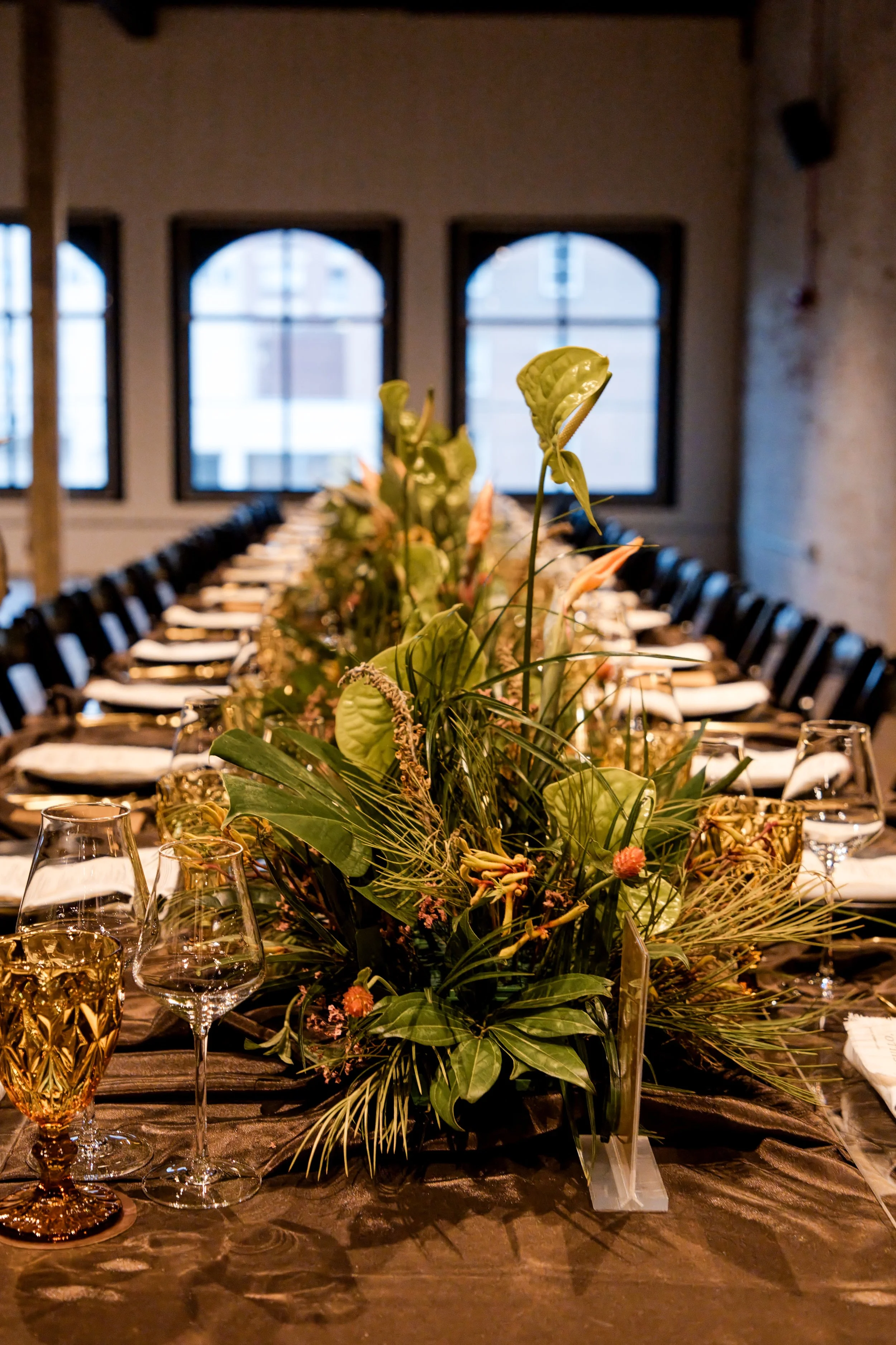 Long dinner table set with greenery centerpieces in an industrial event space