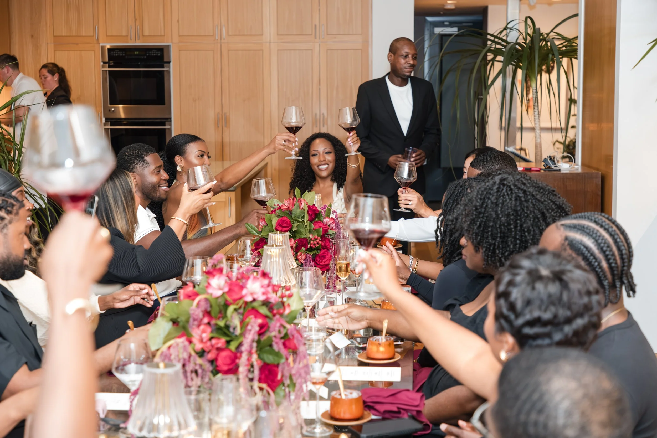 Guests raising glasses around a dinner table with pink floral centerpieces at a private event