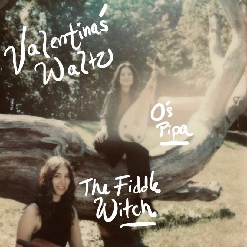 Two women with dark hair outdoors near a large fallen tree; one sitting on the tree holding a Chinese Pipa/ lute and the other holding a nyckelharpa. Handwritten text reads 'Valentina's Waltz', 'O's Pipa', and 'The Fiddle Witch'.