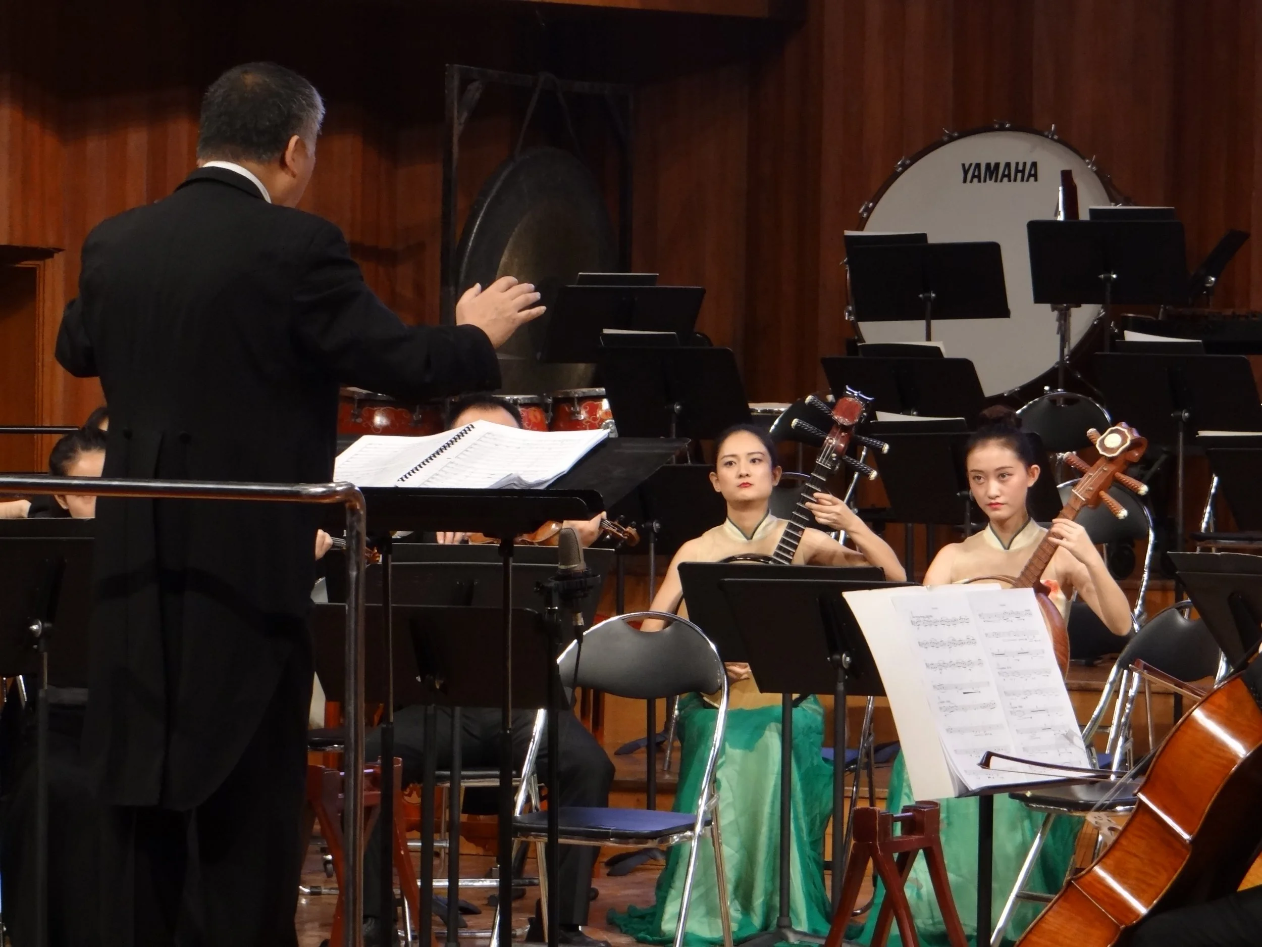 Orchestra conductor leading two female musicians playing traditional string instruments: Ruan/Zhongruan/ Chinese pipa/ Chinese Lute during a concert.