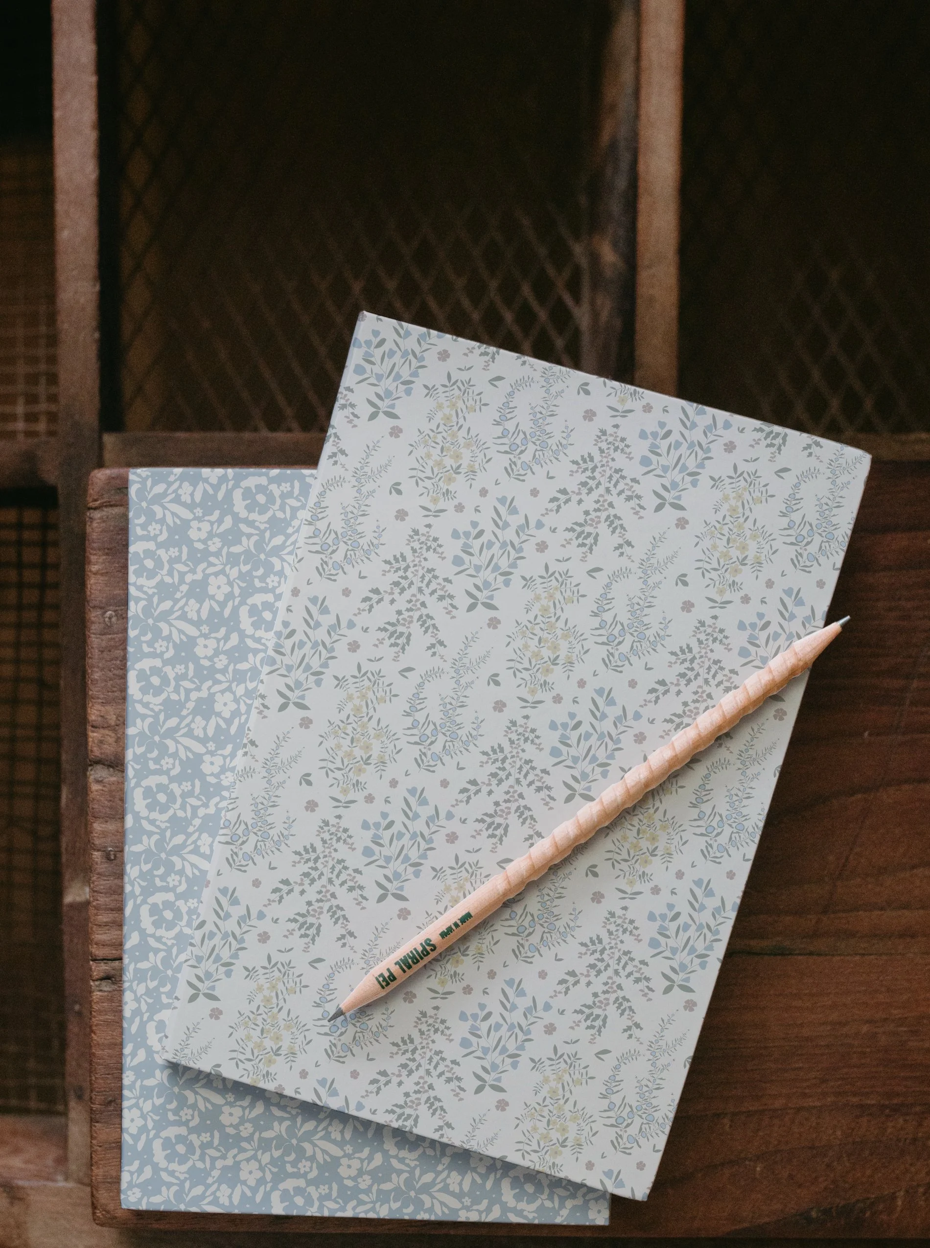 Two sheets of decorative paper with floral patterns, a wooden stick, and a wooden surface with a dark background.