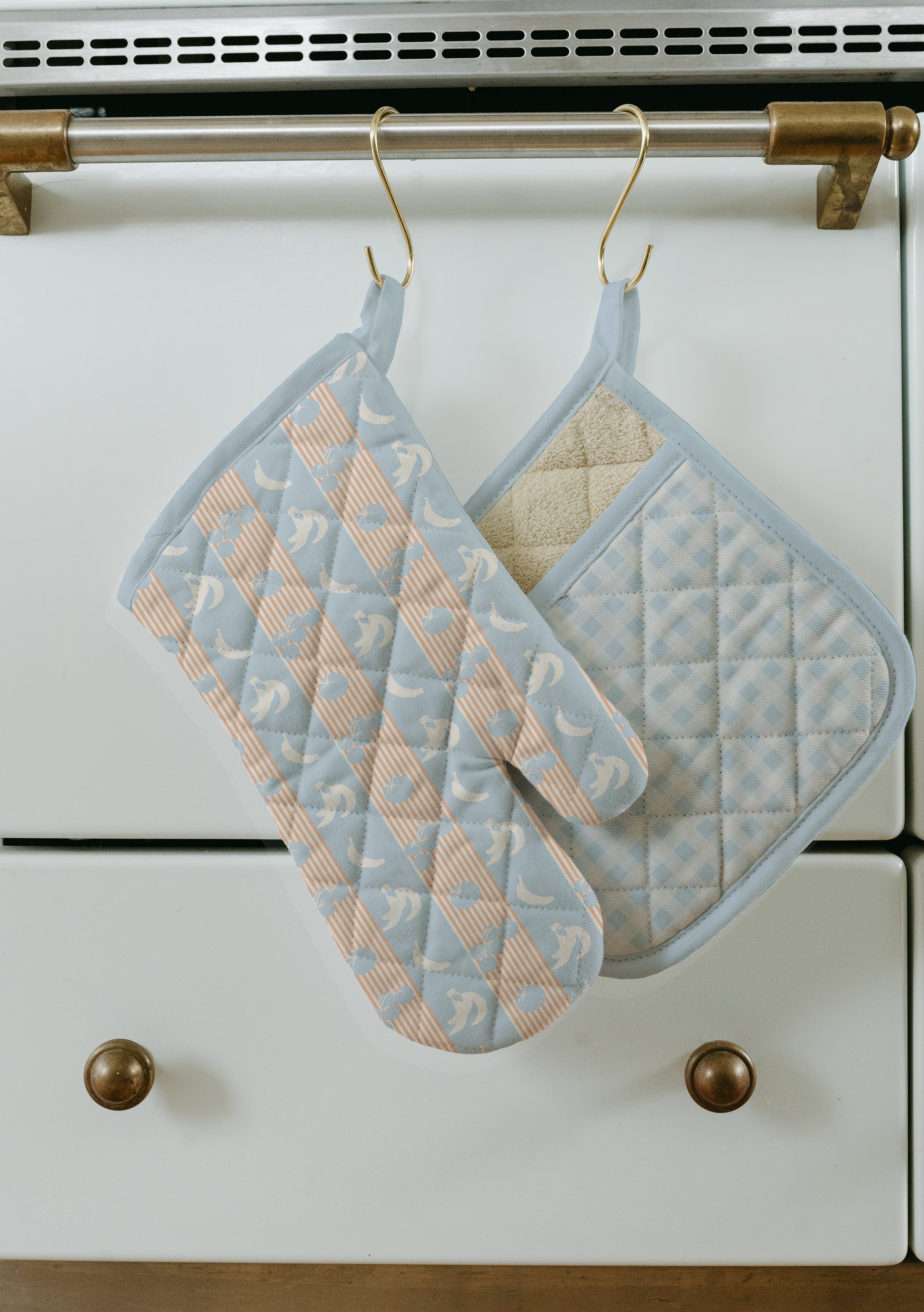Two fabric pot holders hanging on a metal rod in a kitchen.