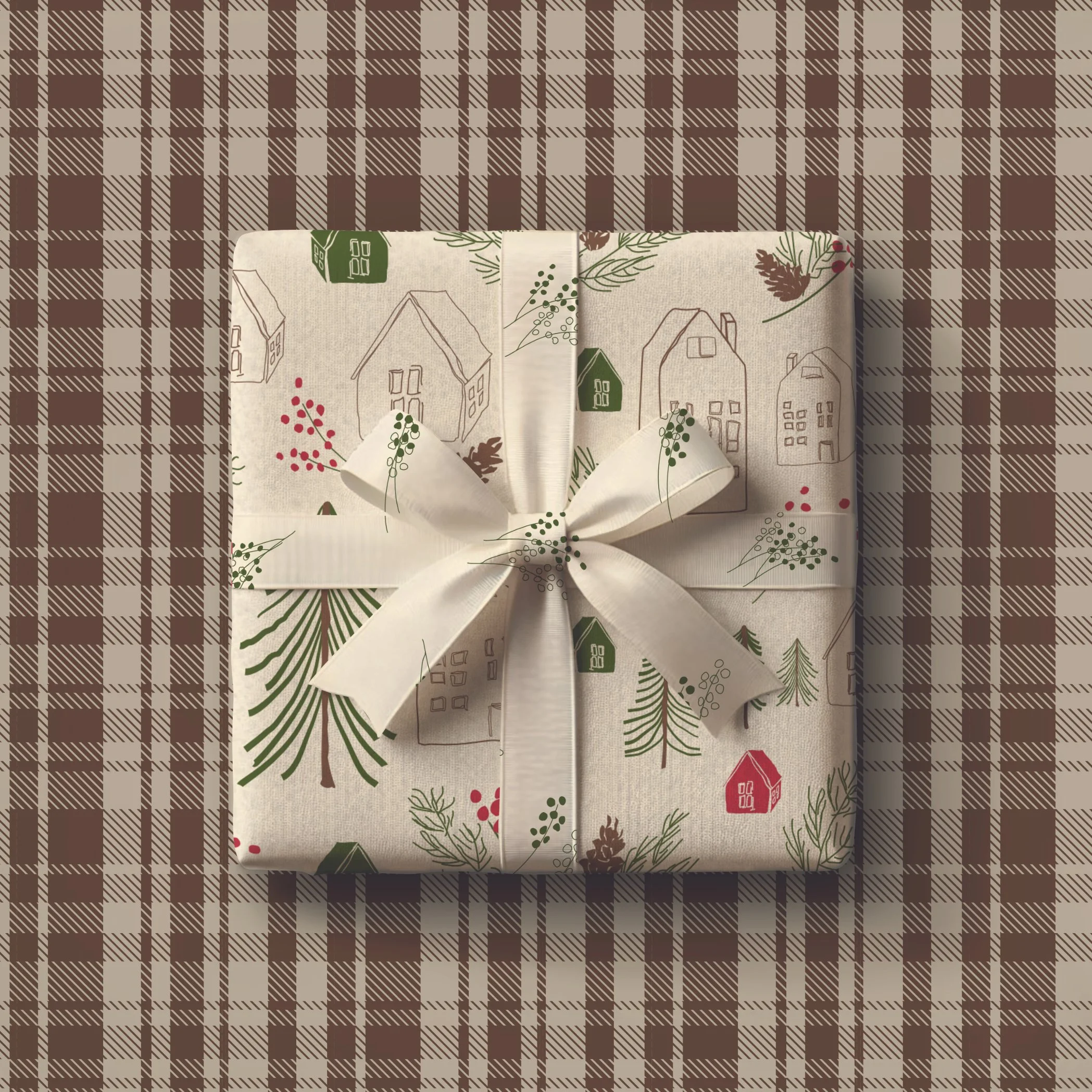Wrapped gift with holiday pattern of houses, pine branches, and red berries, bow on top, on checkered tablecloth.
