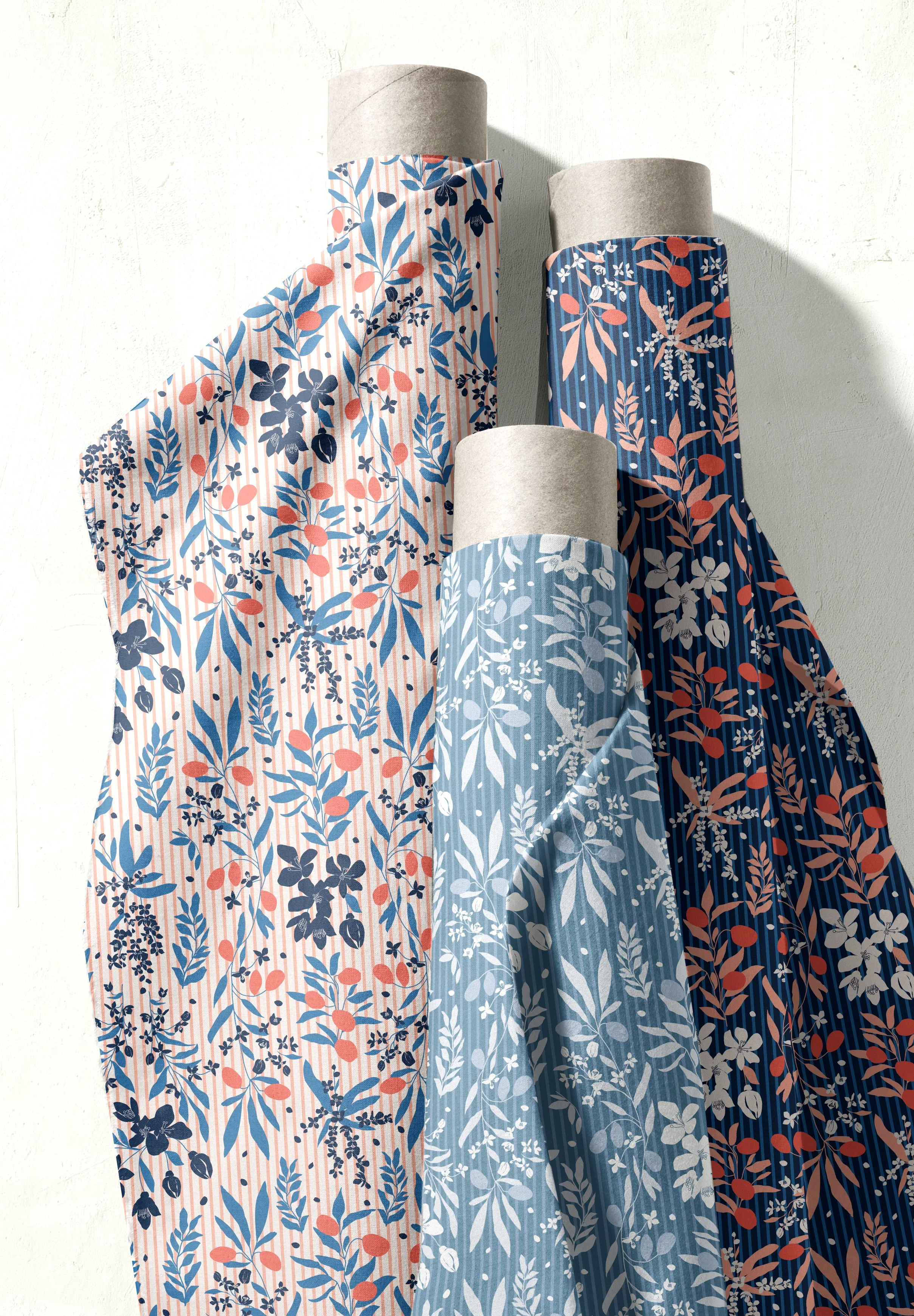 Four rolls of wallpaper with botanical patterns in shades of blue, pink, and white, leaning against a white wall.