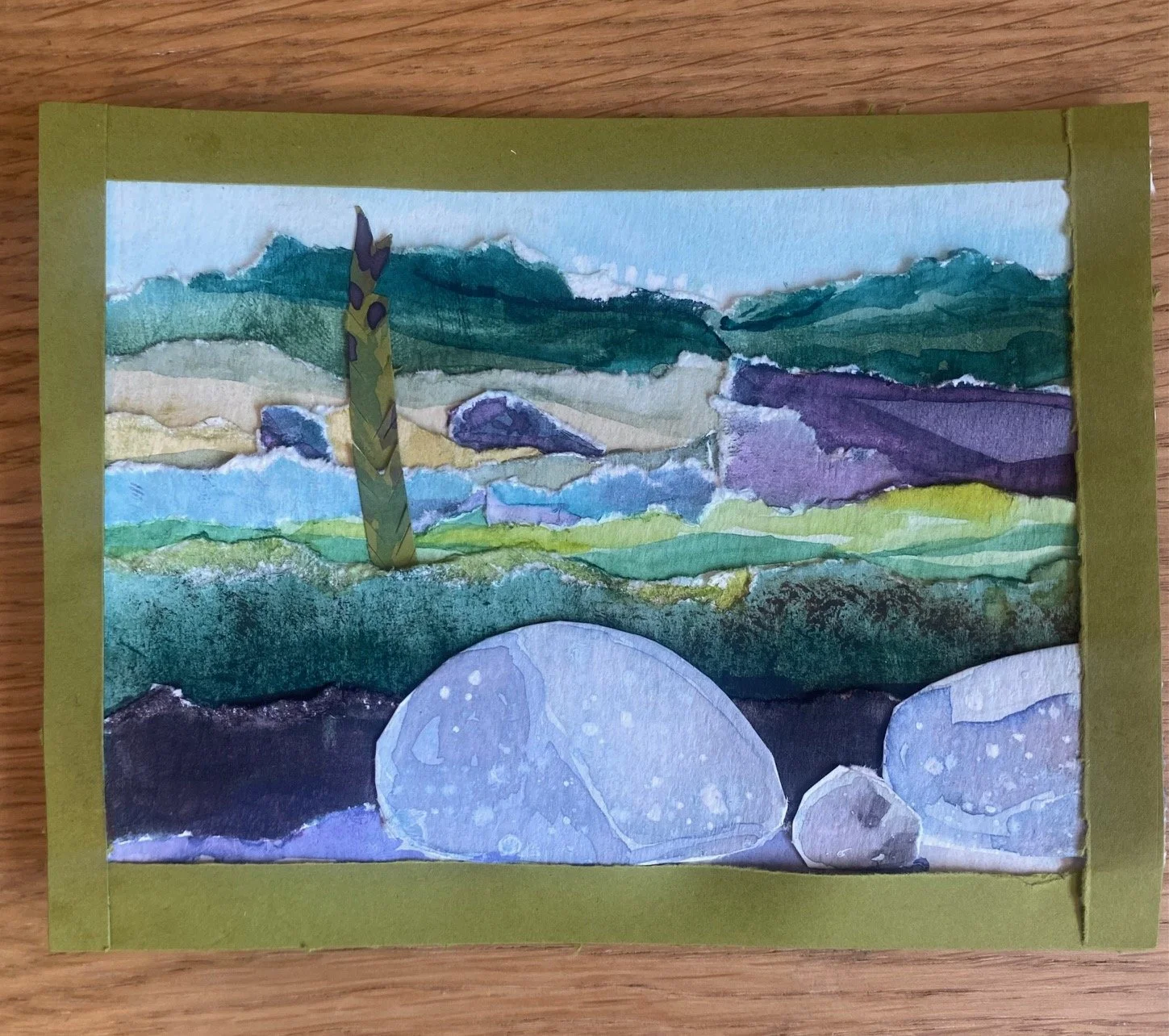 A watercolor painting of rolling green hills and mountains with large rocks in the foreground and a cloudy sky.