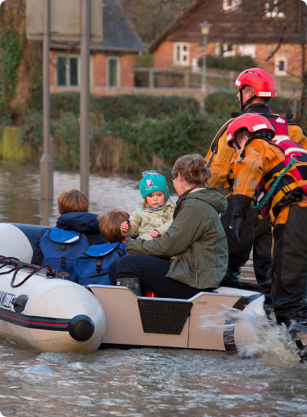 Rescue team in life jackets helping children and a woman in a small boat on a flooded street.