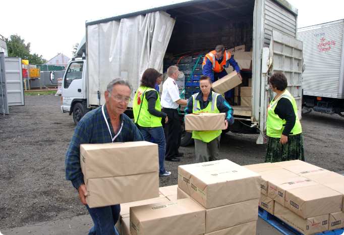 People in safety vests unload large boxes from a delivery truck.