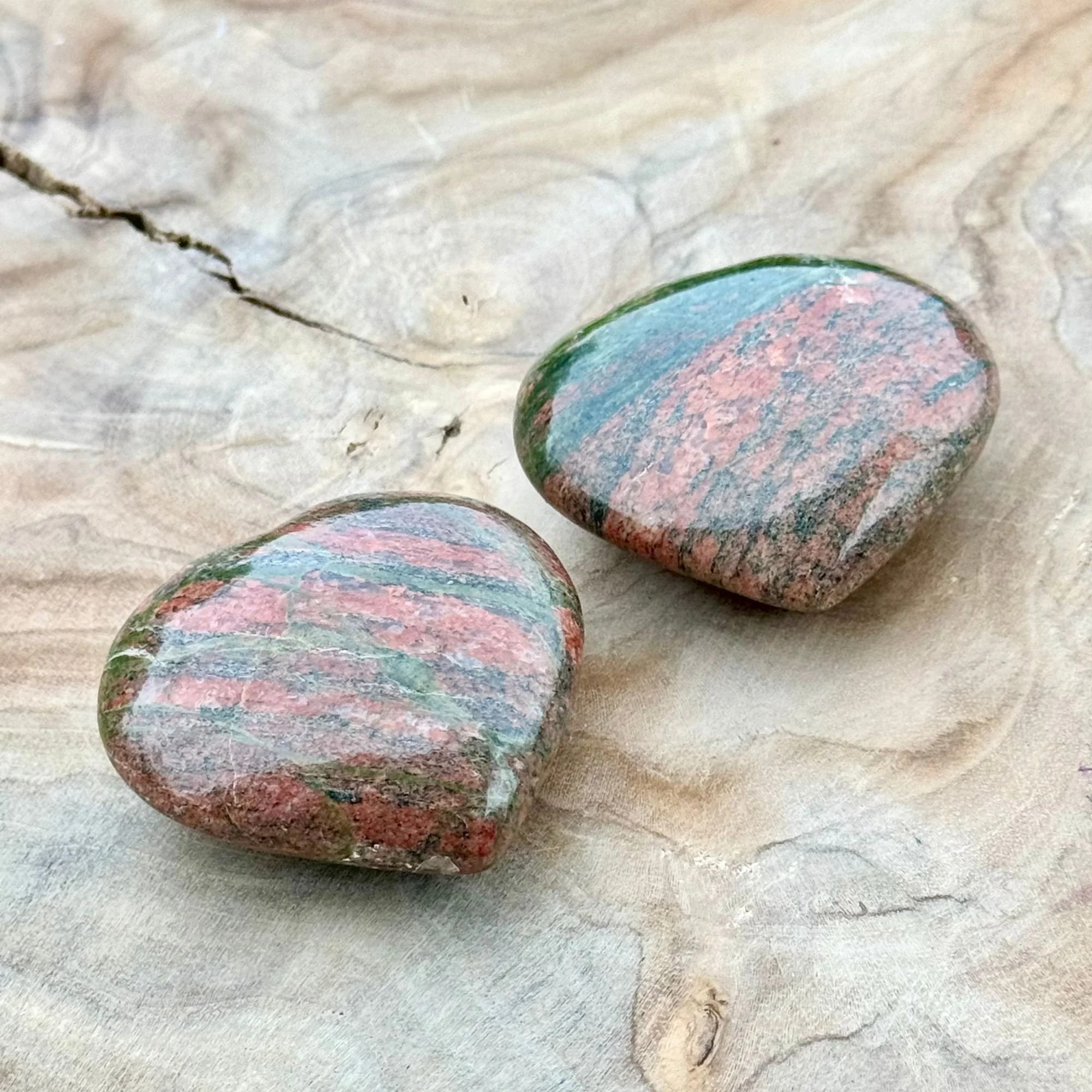 Two Unakite Jasper Hearts featuring natural patterns of dark olive green and pink/red displayed on a wooden dish