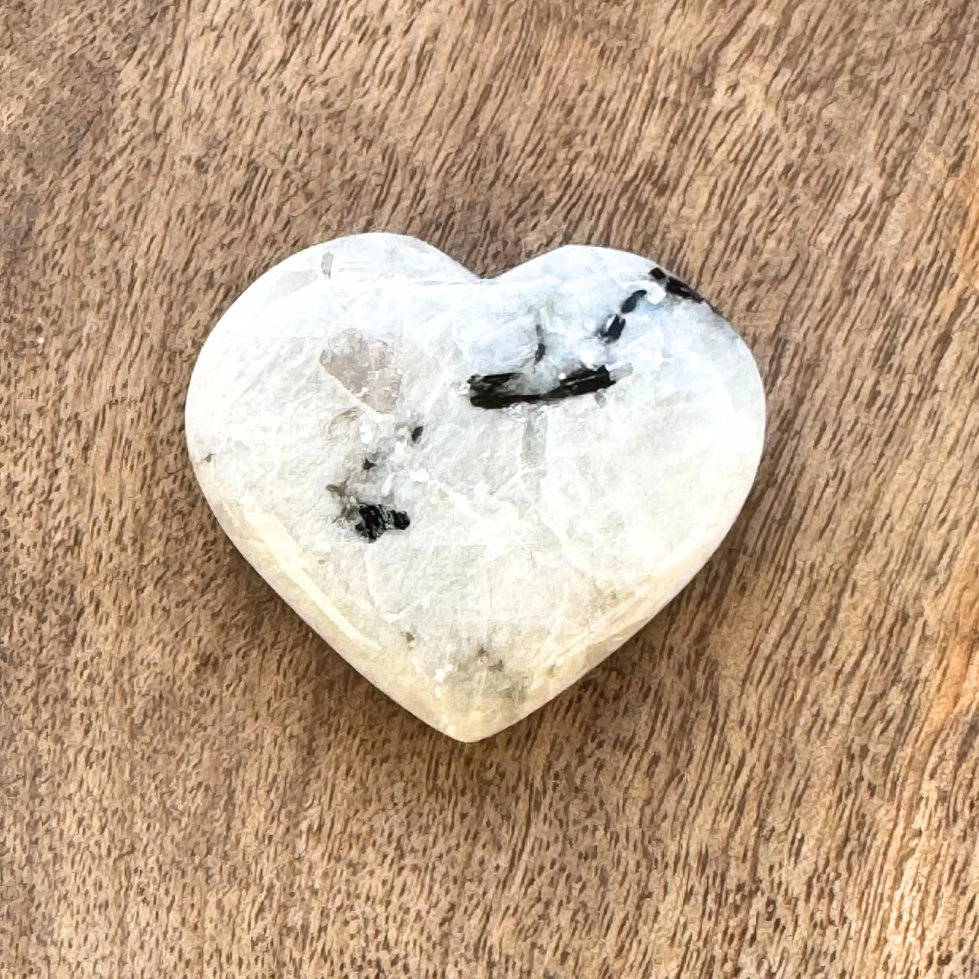Close up view of a Rainbow Moonstone Heart Carving on a wooden surface
