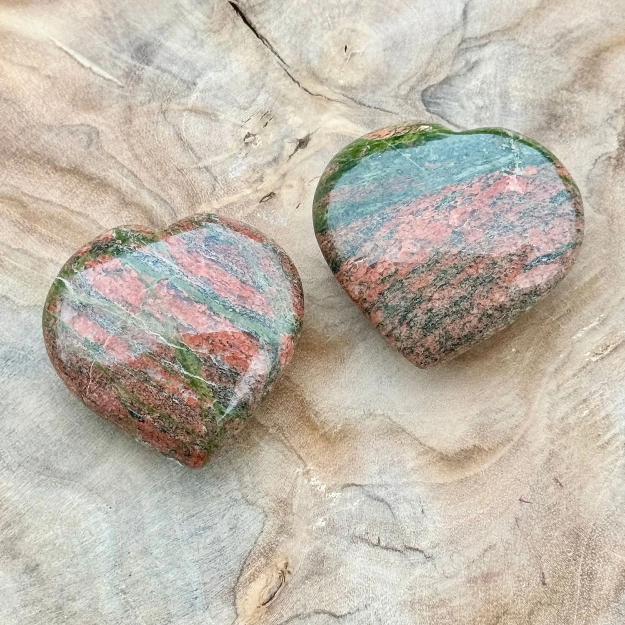 Two Unakite Jasper Hearts featuring natural patterns of dark olive green and pink/red displayed on a wooden dish