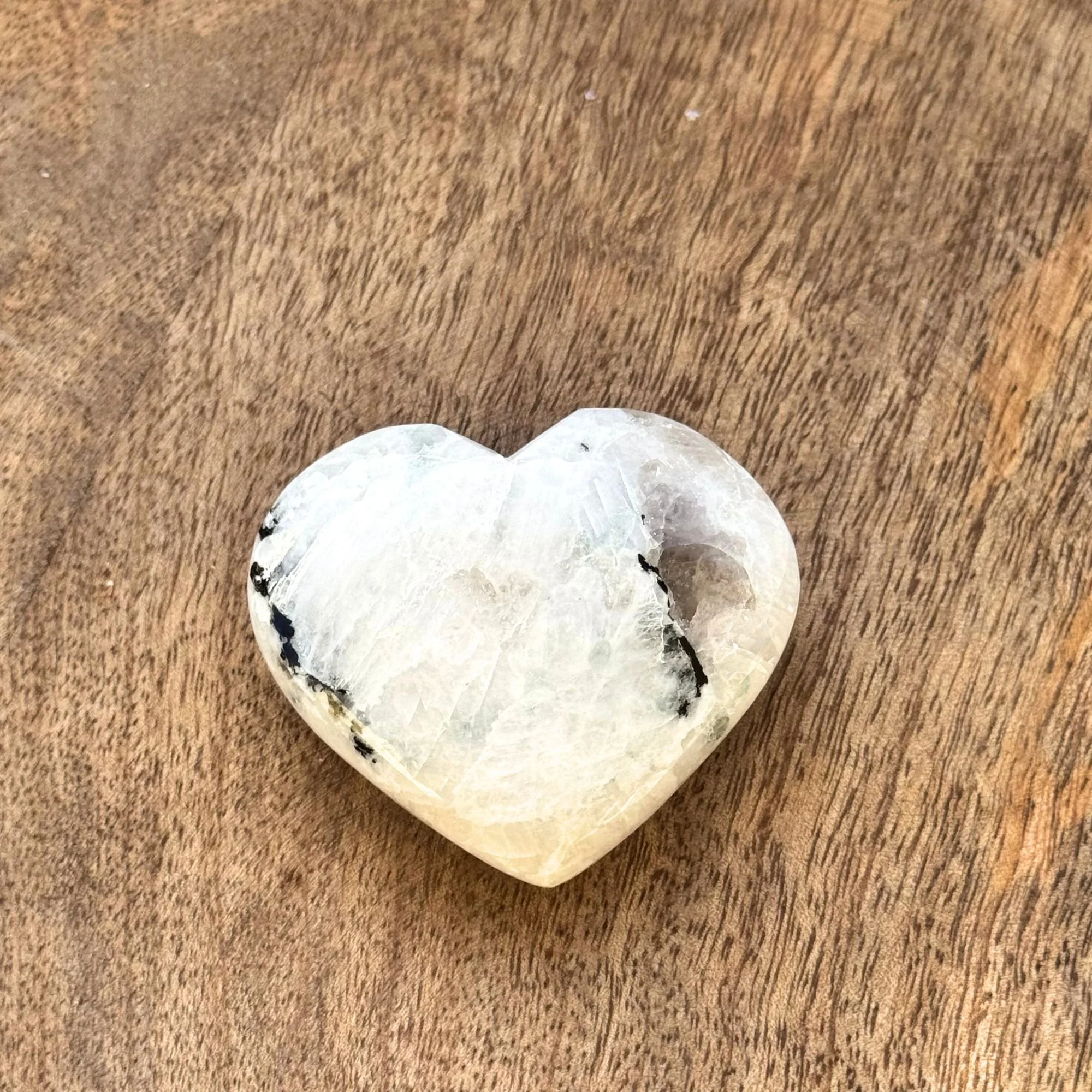 other side view of a Rainbow Moonstone Heart Carving on a wooden surface