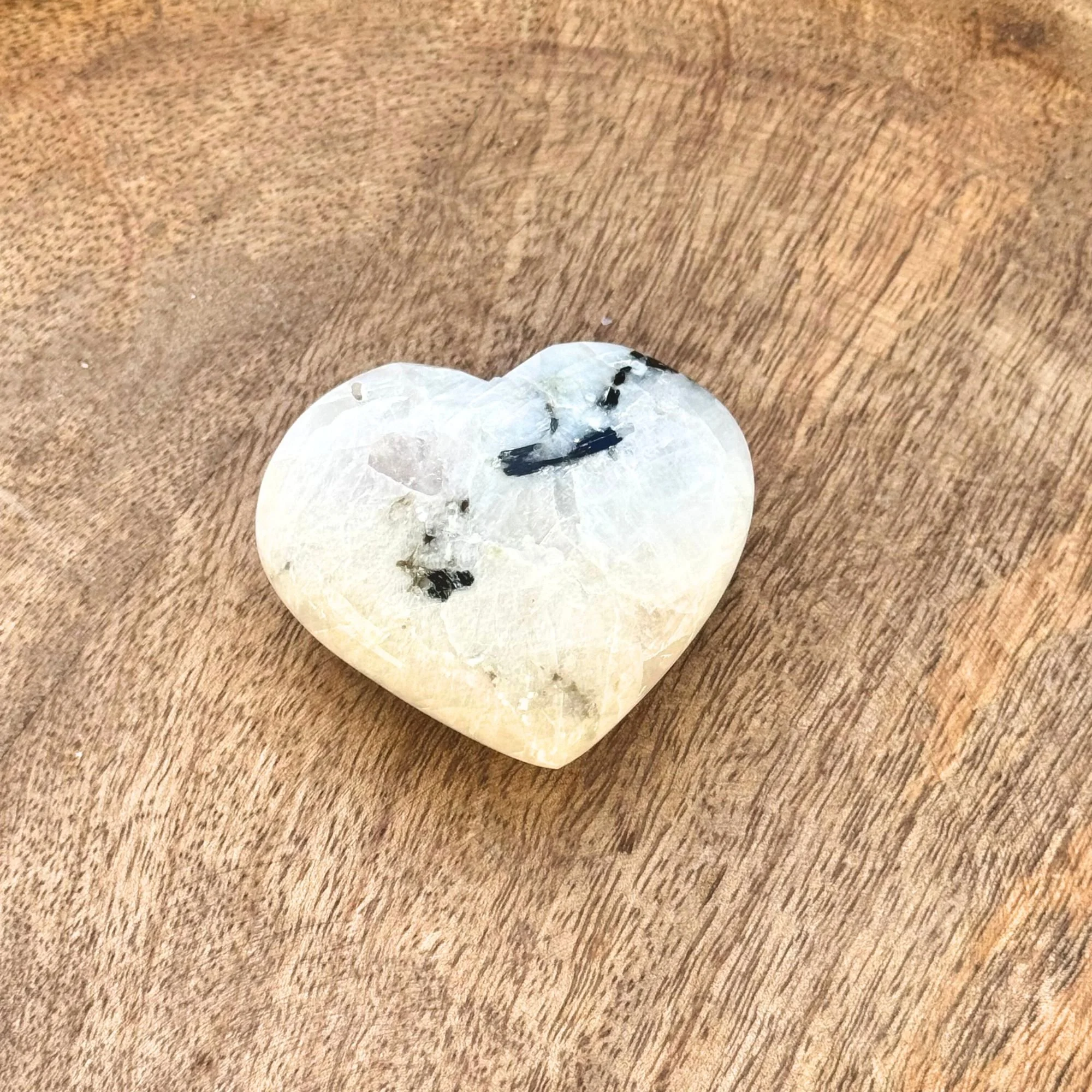 Rainbow Moonstone Heart Carving on a wooden surface