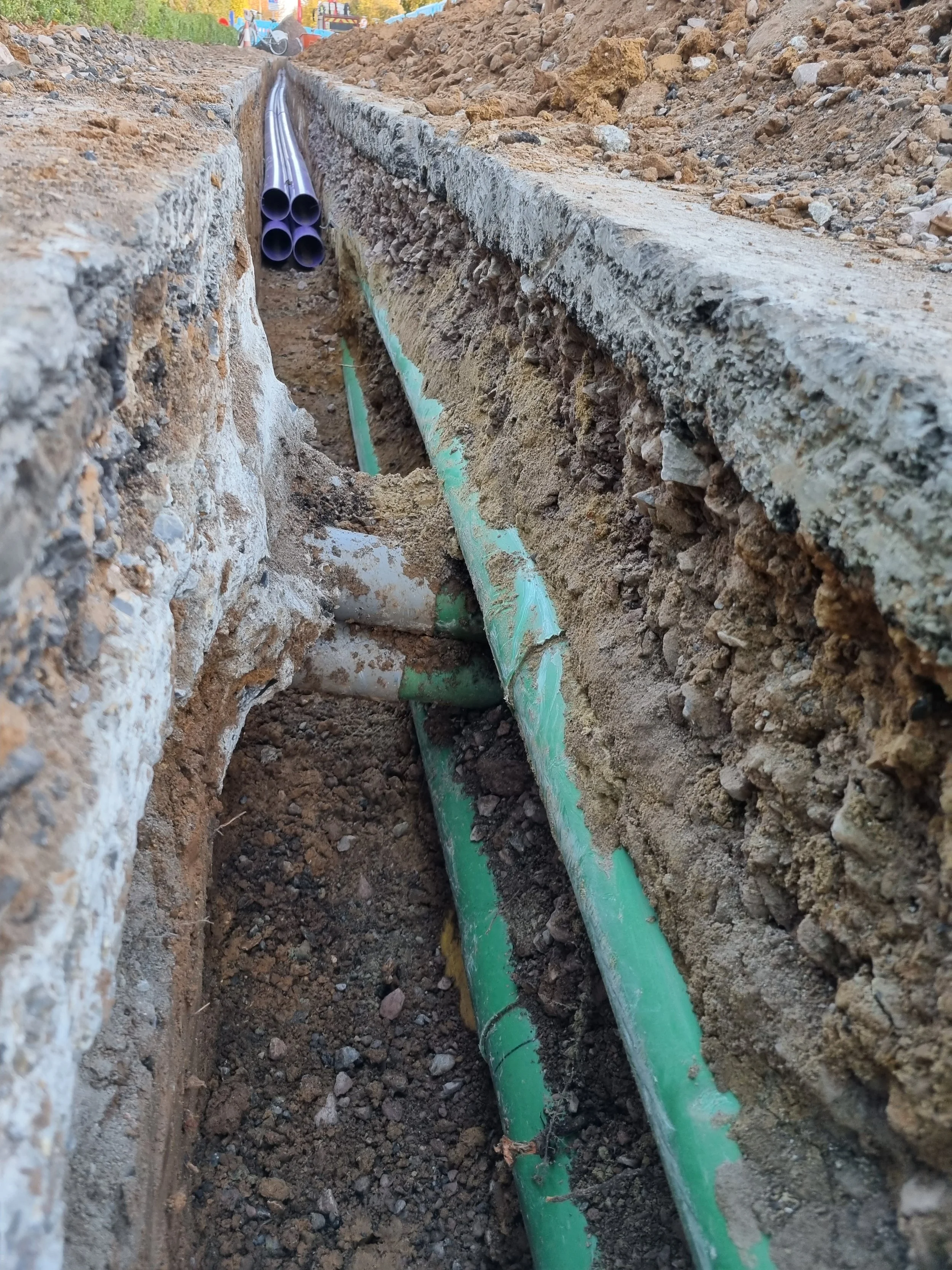 Underground green pipes in a trench under construction, with visible dirt and gravel around them.