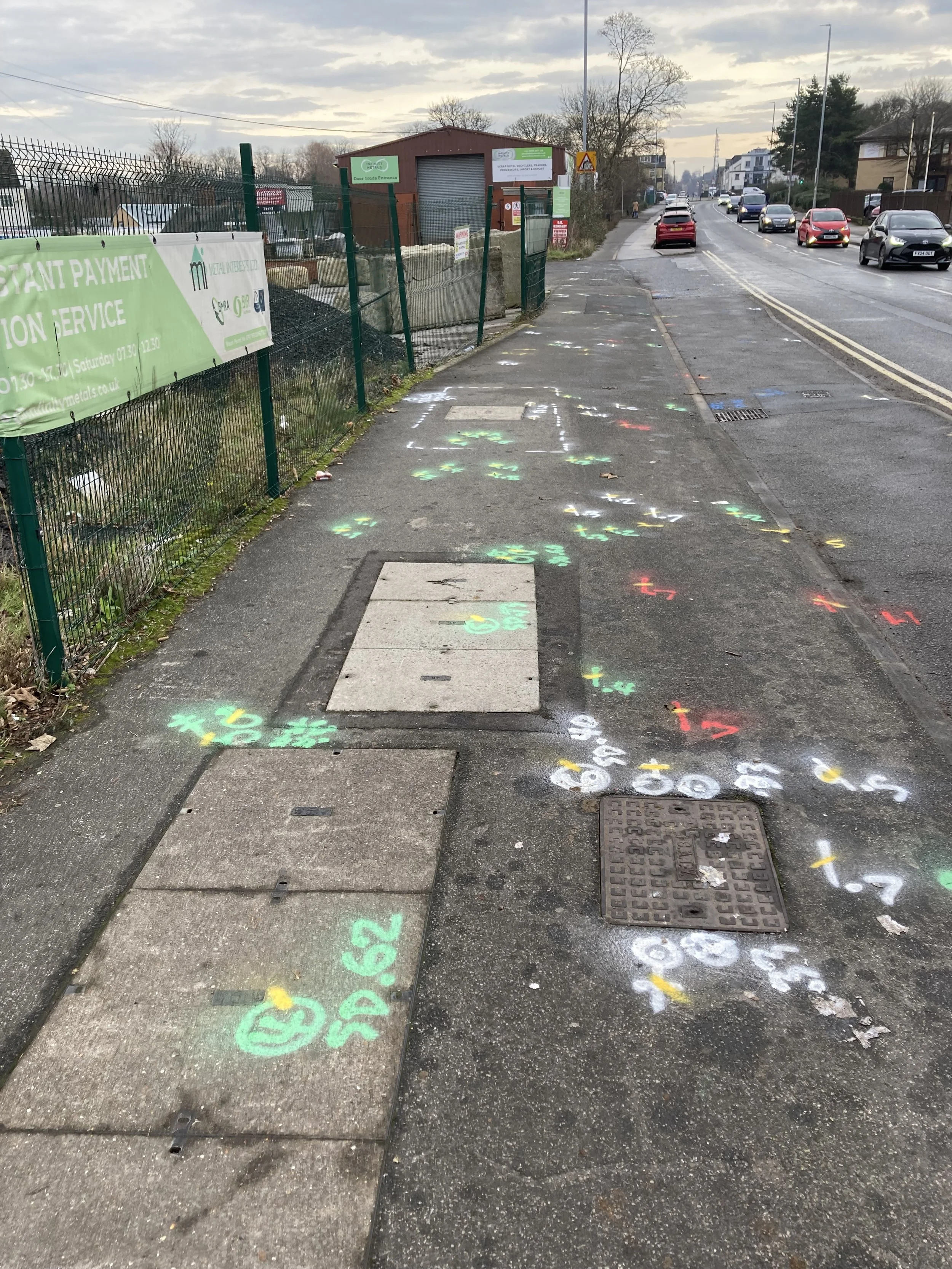 Colorful painted numbers and symbols on the sidewalk, with a road and parked cars in the background.