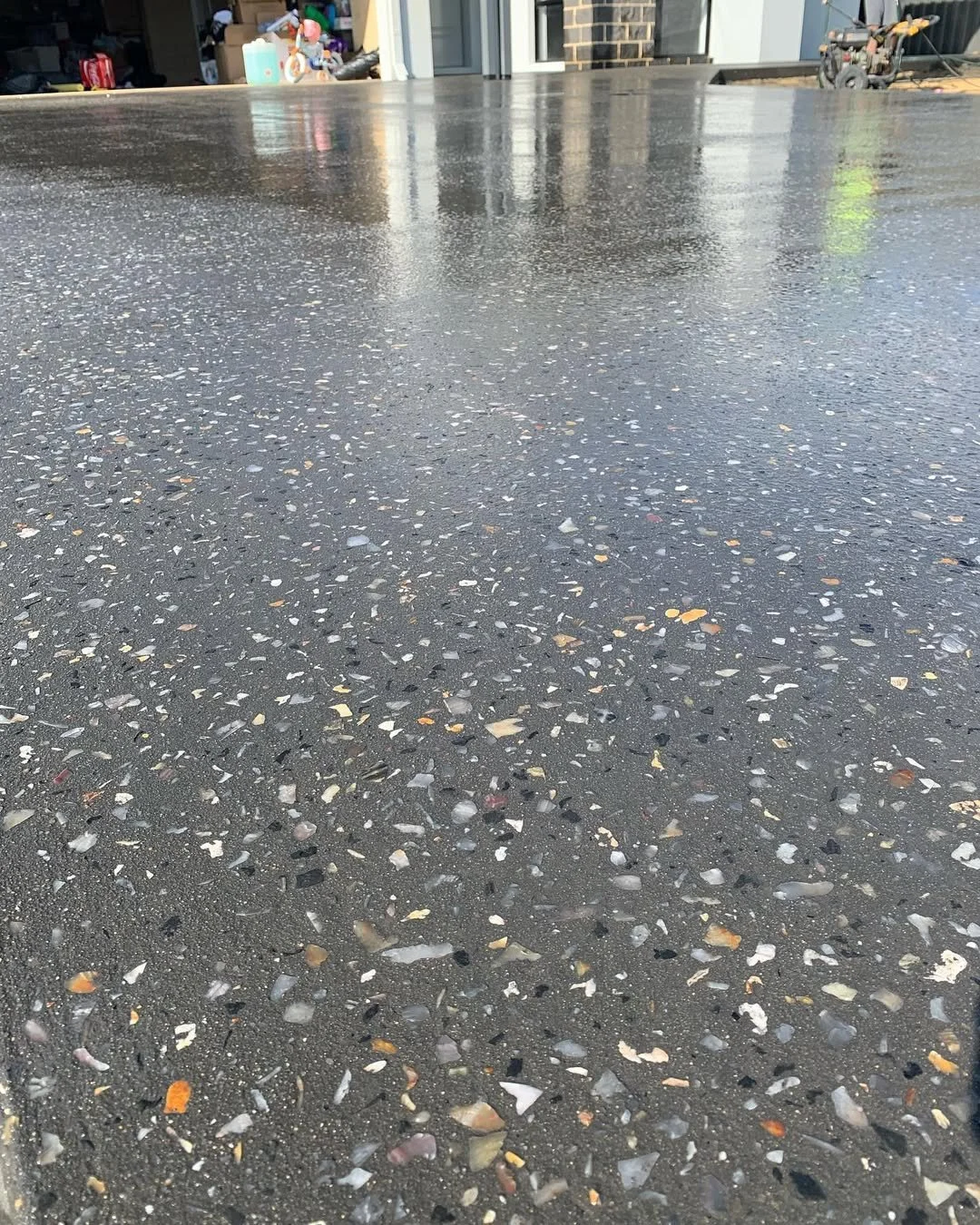 Close-up of a wet, polished concrete floor with colorful aggregate chips embedded in it.