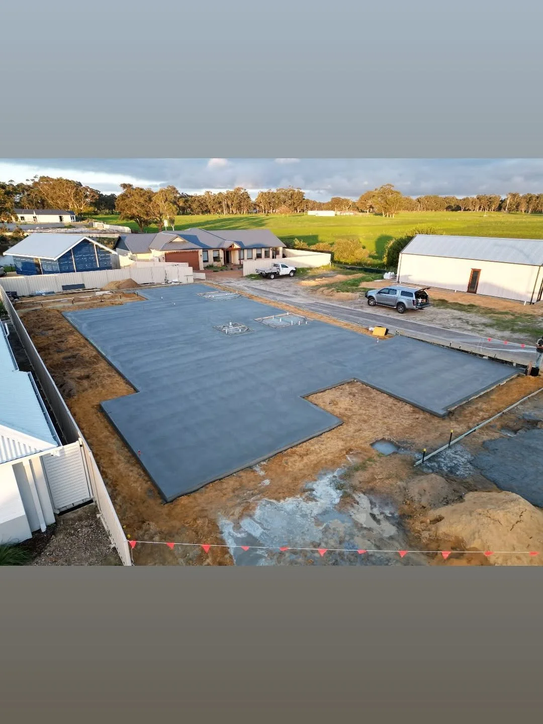 Concrete foundation slab at a construction site with a rural landscape in the background.