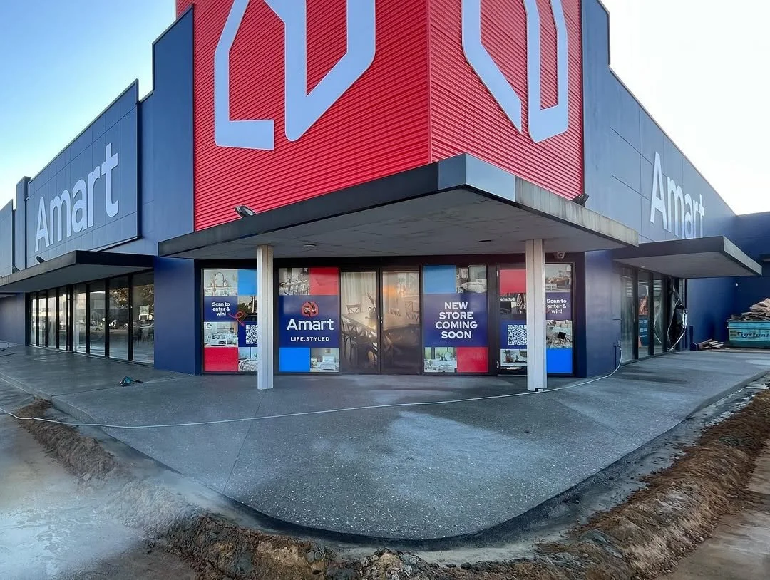 Exterior of an Amart store under construction, with signs indicating a new store opening soon, and a large Amart logo on the building.