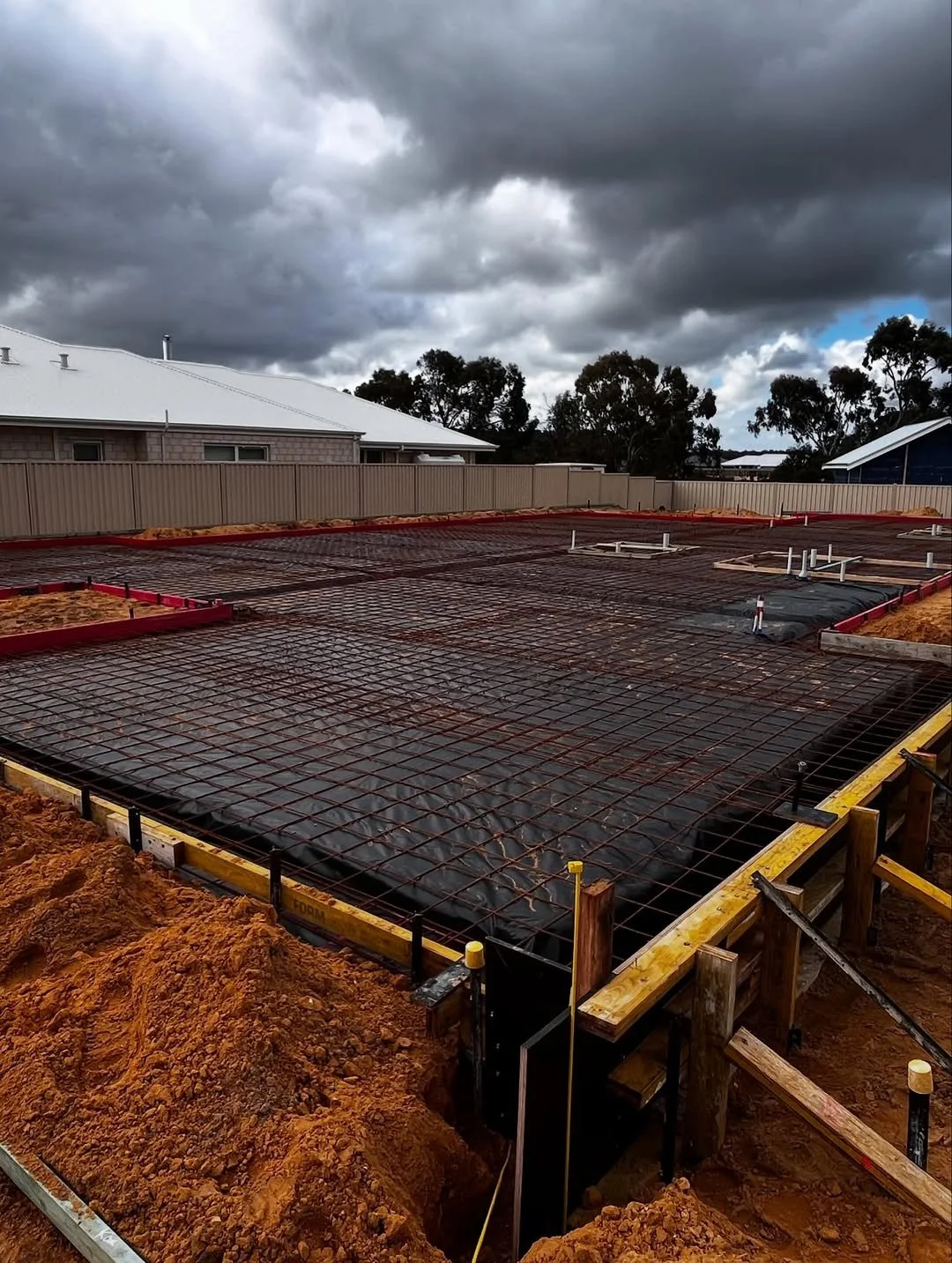 Construction site with concrete foundation and rebar, overcast sky with dark clouds.