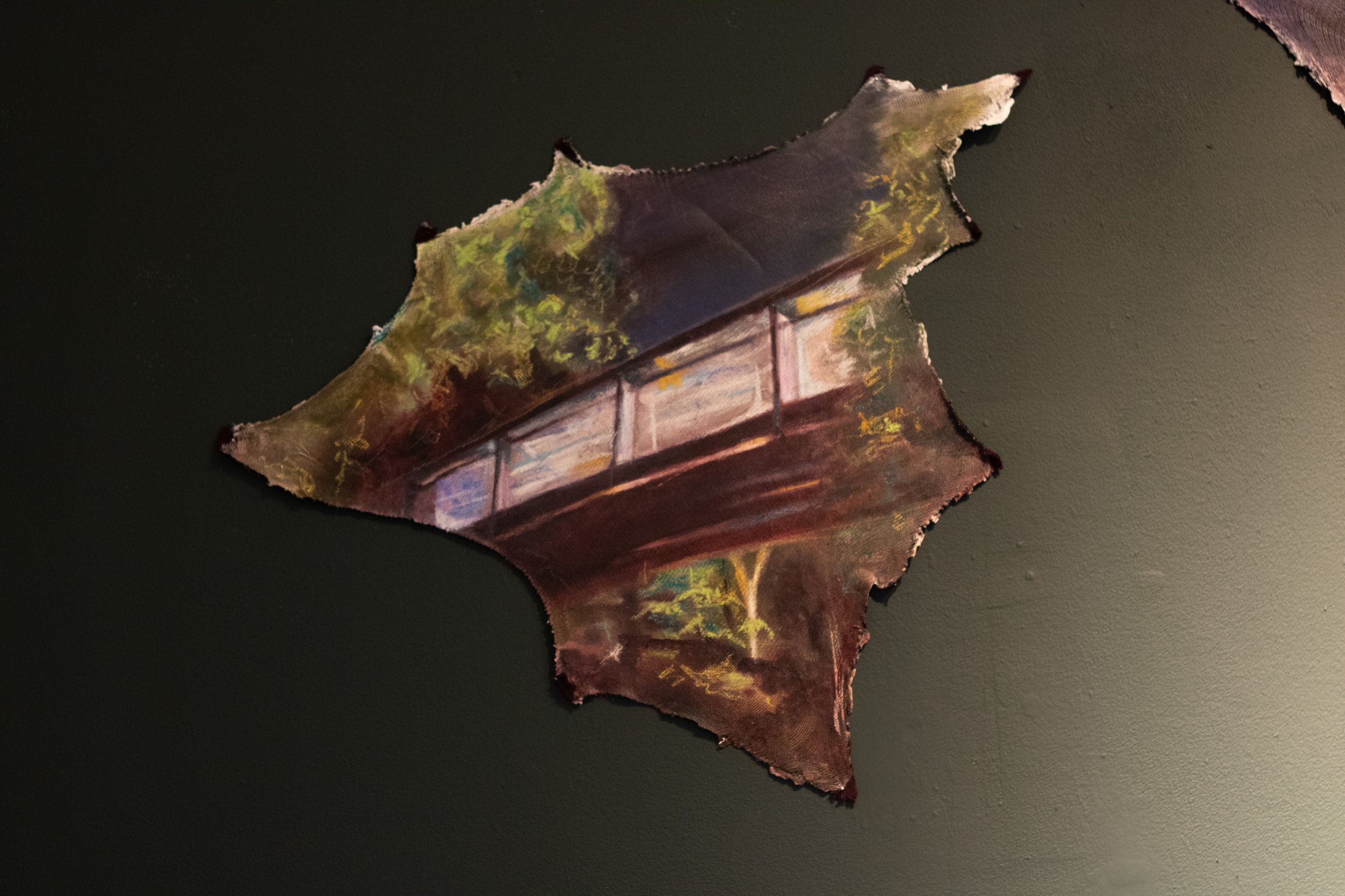 A leaf with a painted or printed image of a bridge and trees on it, placed on a dark surface.