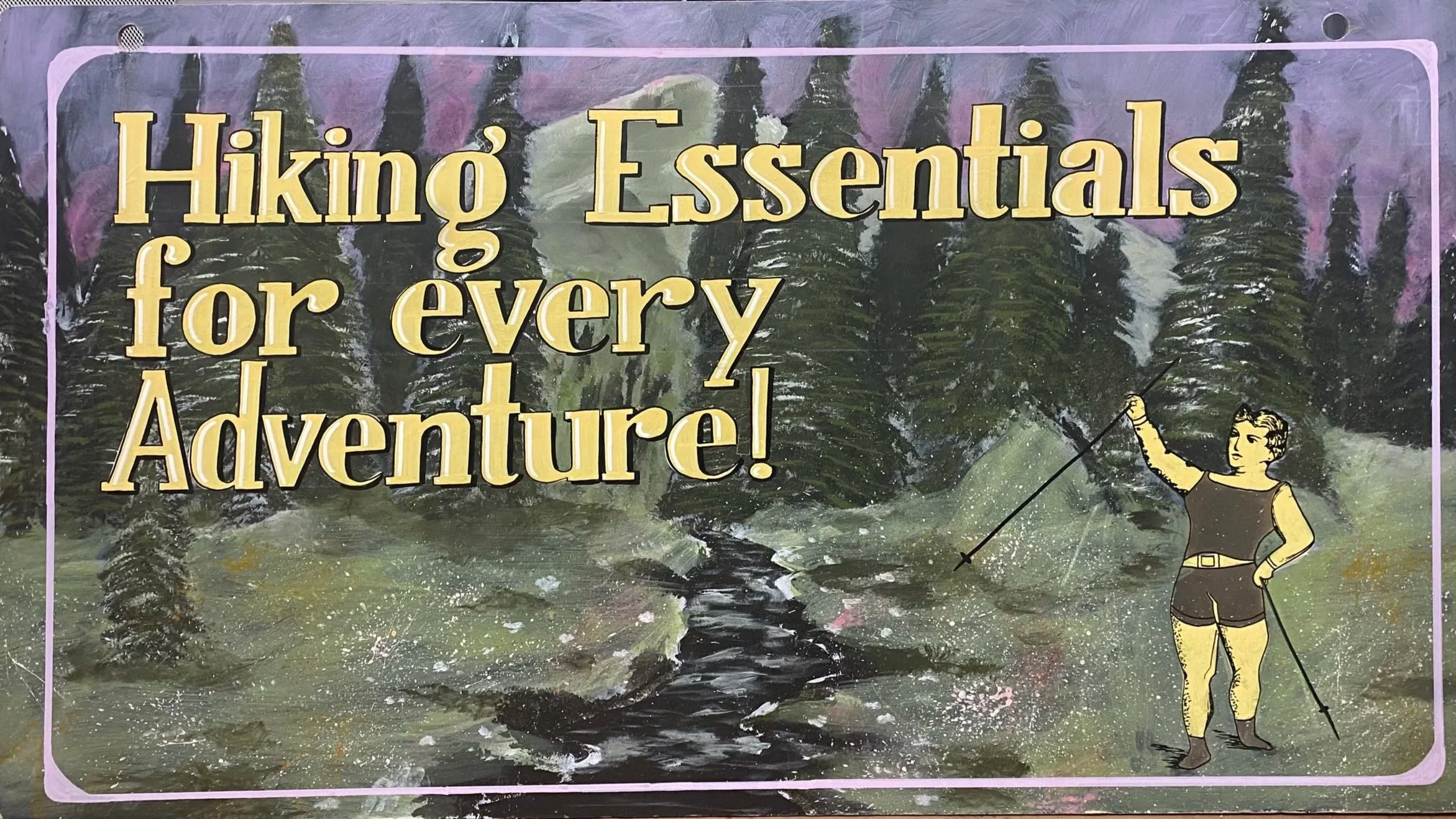 An end-cap sign with the text 'Hiking Essentials for every Adventure!' set against a background of a forest with tall pine trees and a meandering stream. There is an illustration of a woman in hiking gear holding a walking stick on the right side.