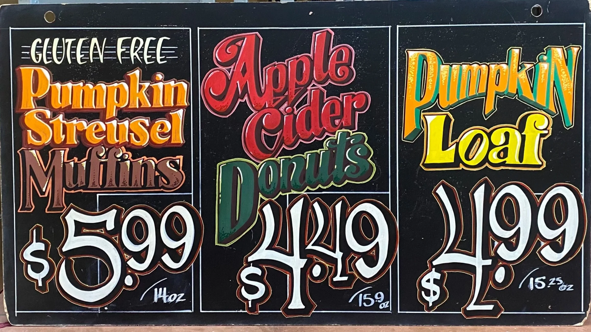 A end-cap sign displaying gluten-free options including pumpkin streisel for $5.99, apple cider donuts for $4.99, and pumpkin loaf for $2.99, with prices marked per 1, 1.5, and 1.25 ounces respectively.
