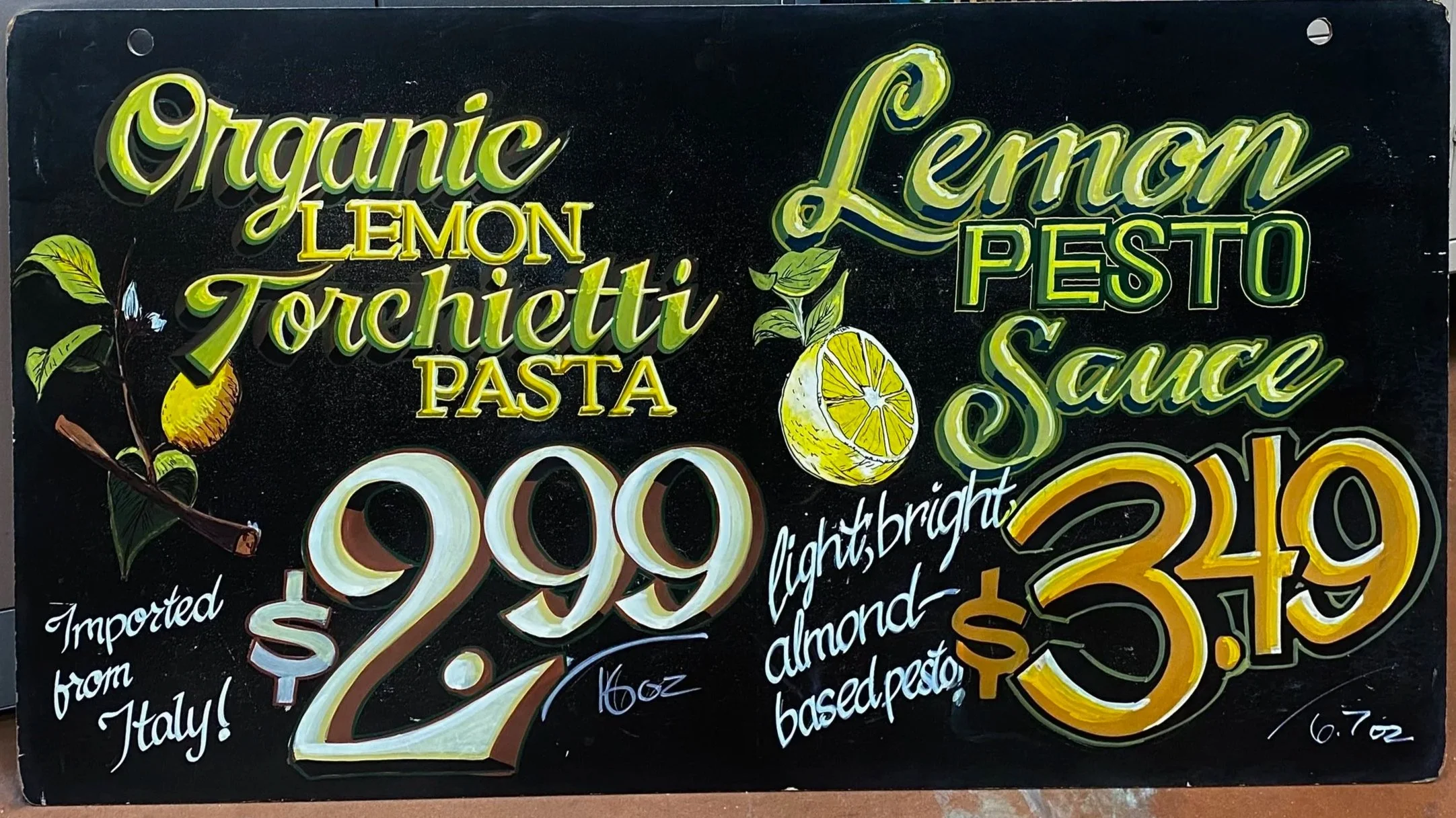 A end-cap sign advertising organic lemon torchietti pasta for $2.99 per 16 ounces, imported from Italy, with lemon pesto sauce for $3.49, emphasizing bright, light almond-based pesto.