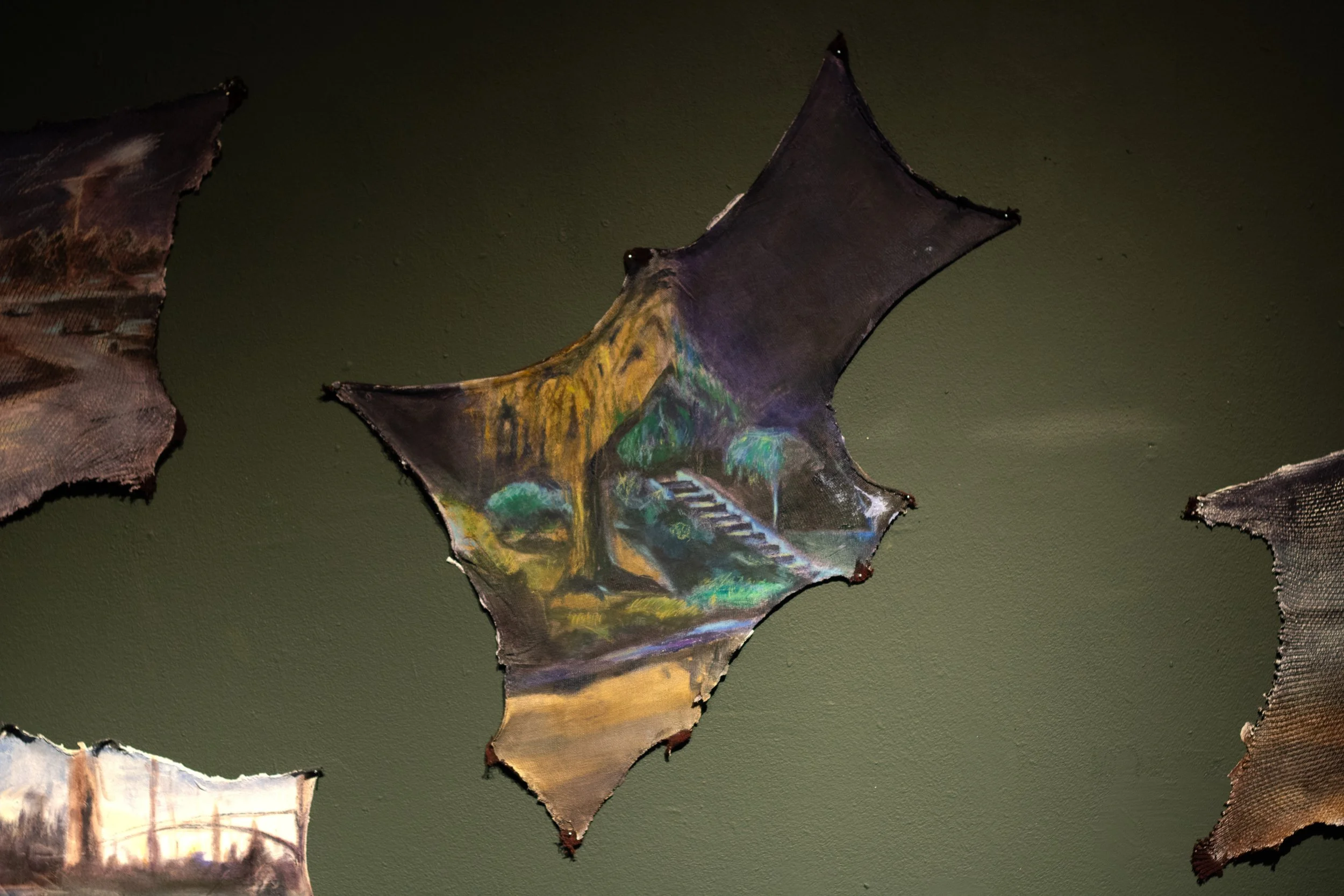 Colorful artwork painted on a torn piece of dark-colored material resembling a leaf.
