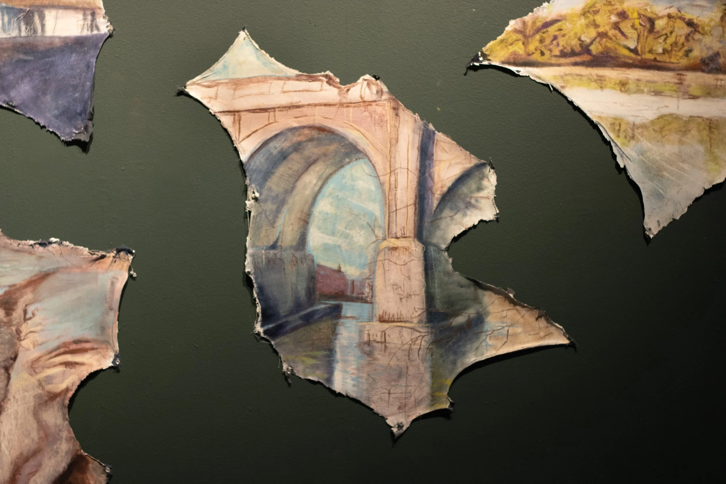 Torn pieces of paper with watercolor paintings, including a bridge over a river, on a dark background.
