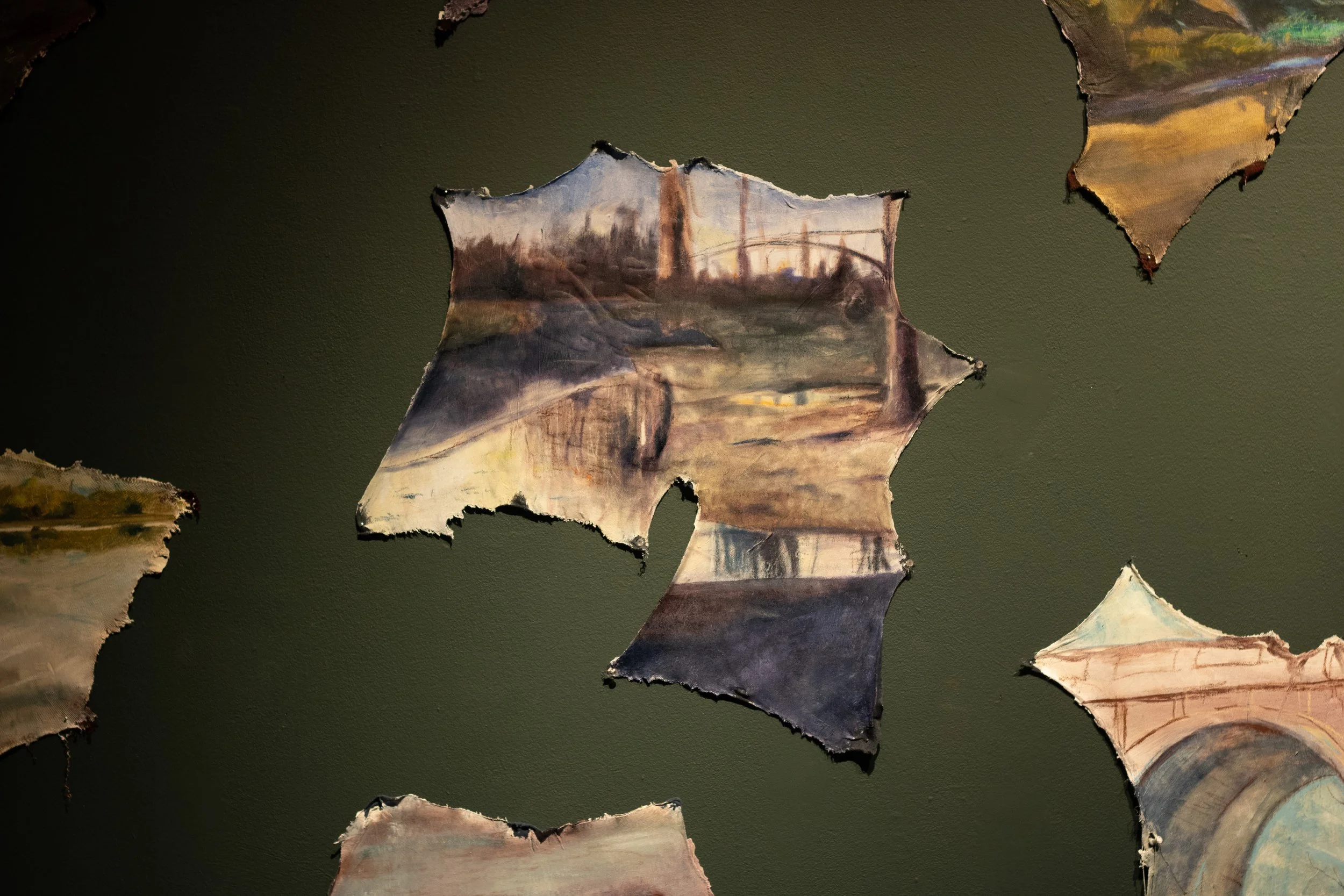Fragments of torn painted canvas with landscape scenes, suspended against a dark background.