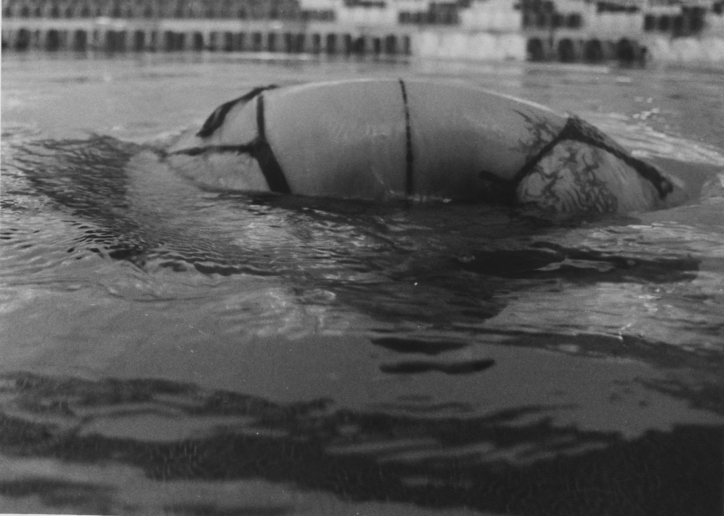 A person swimming in a pool wearing goggles and a swimsuit, with the focus on their head submerged in water and swimming towards the surface.