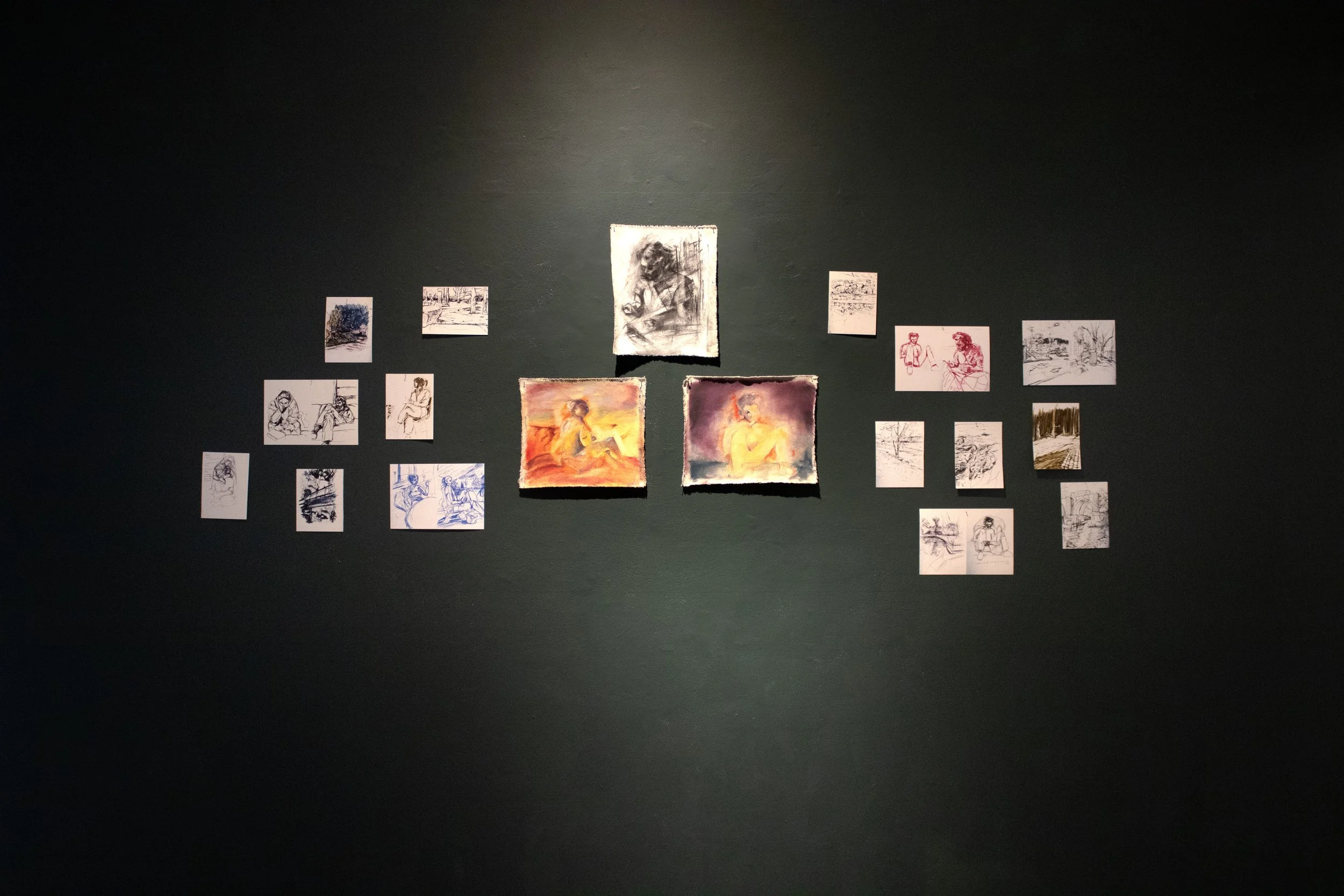 Wall display of multiple sketches and paintings, including portraits and landscape scenes, arranged in a loose symmetrical pattern.