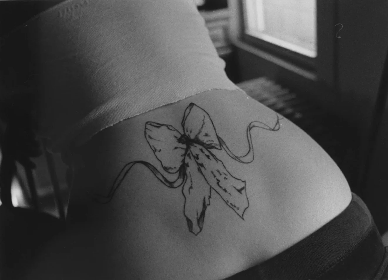 Tattoo of a butterfly with a bow on a person's side, black and white photograph