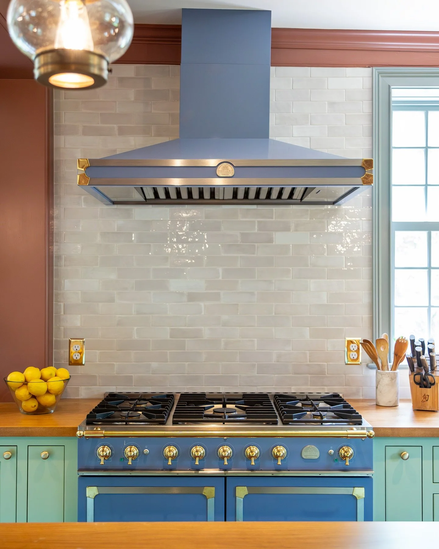Colorful kitchen with a blue stove and matching vent hood, white tile backsplash, lemon bowl on the left, and wooden utensils in a marble container on the right. Heartwood Renovations. West Hartford, CT