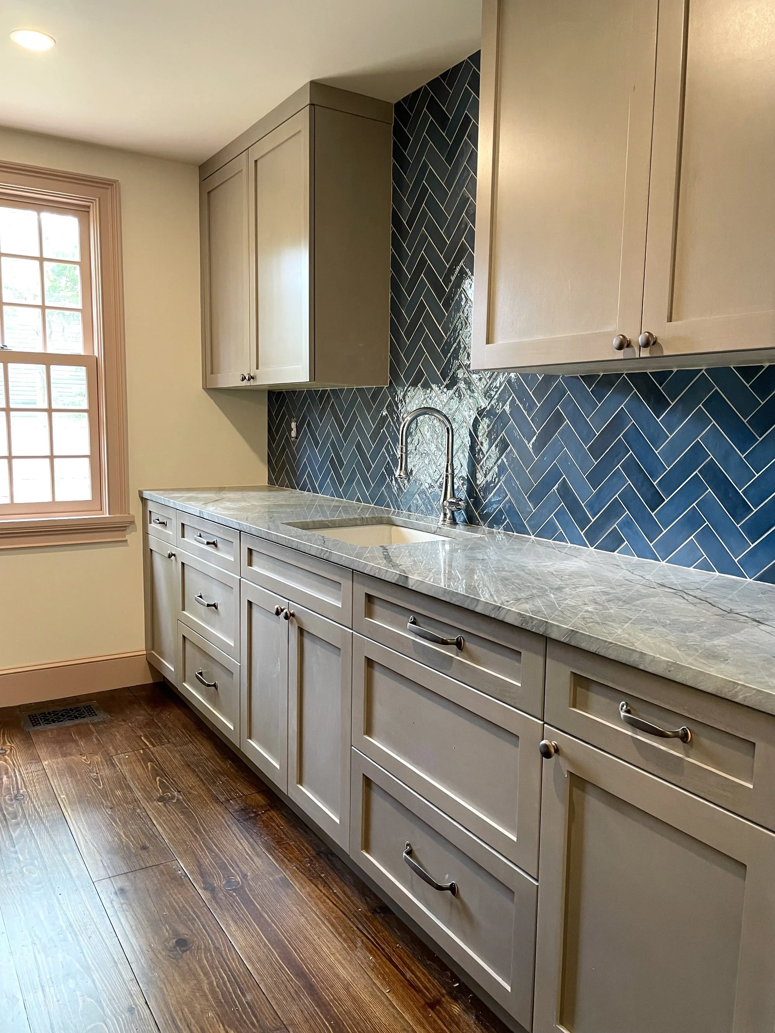 Kitchen with beige cabinets, marble countertop, blue herringbone tile backsplash, and wooden flooring. Heartwood Renovations. West Hartford, CT
