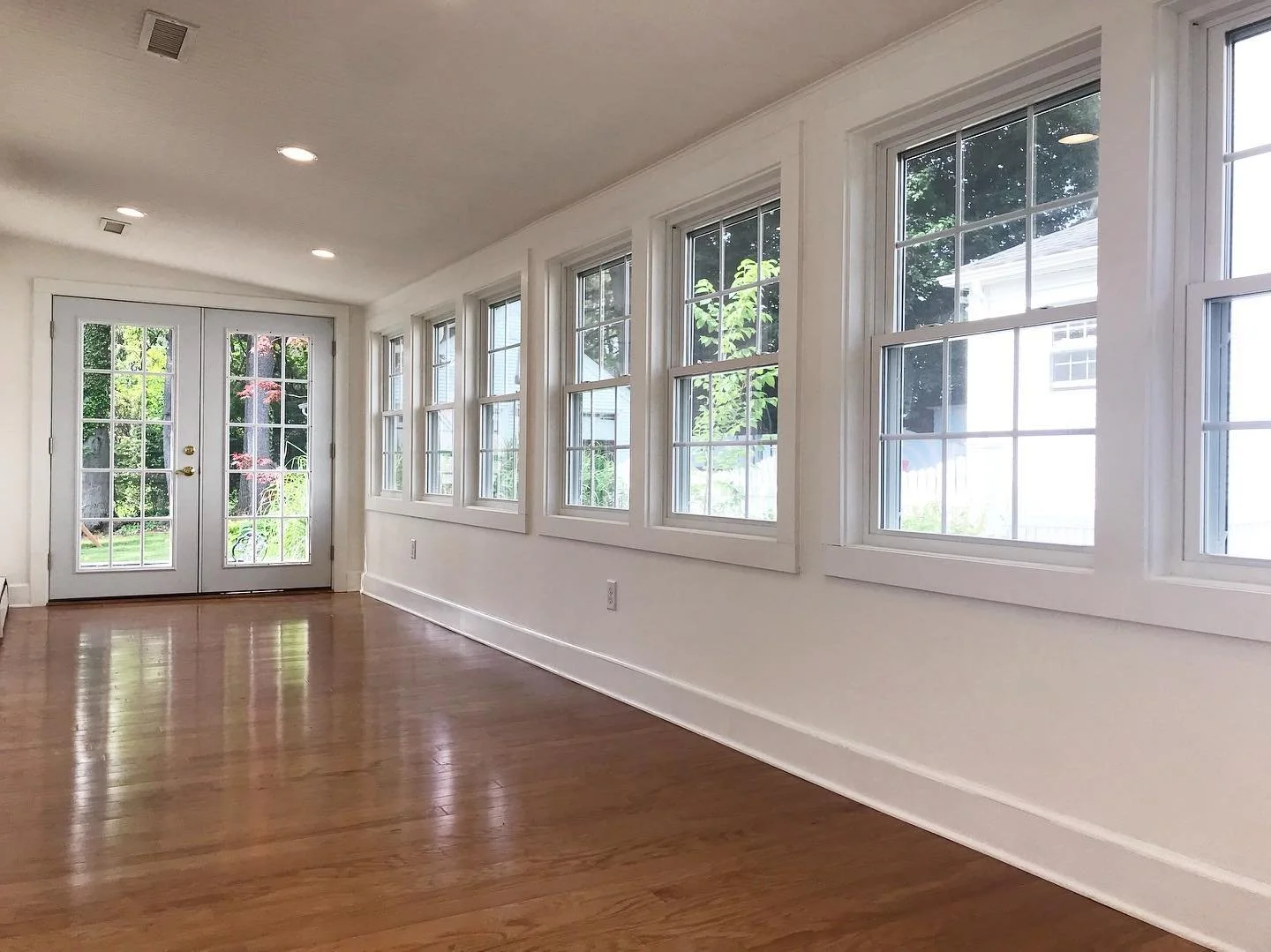Empty sunroom with large windows, white walls, hardwood floors, and double glass doors leading outside. Heartwood Renovations. West Hartford, CT