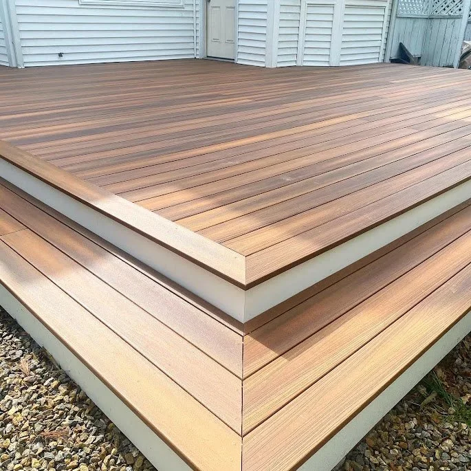 A wooden deck with horizontal planks and a raised border, located outside a house with light blue siding and a white door. Heartwood Renovations. West Hartford, CT