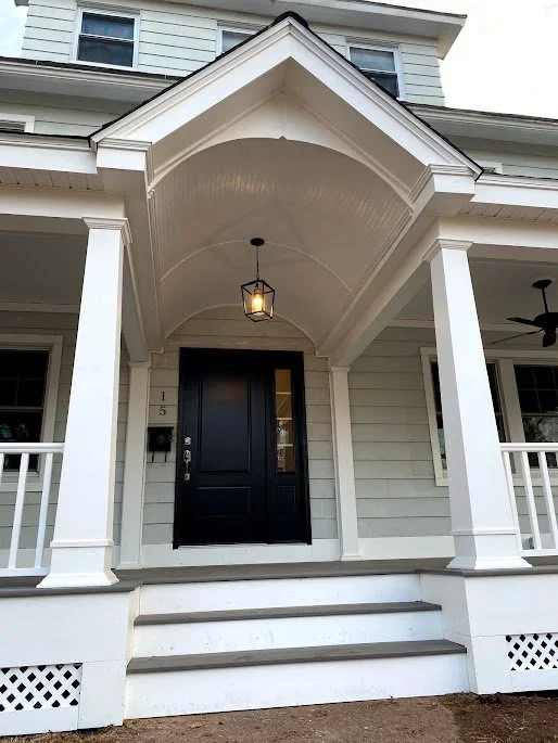 Front porch of a house with white columns, a black door, and an arched roof with a hanging lantern light. Heartwood Renovations. West Hartford, CT