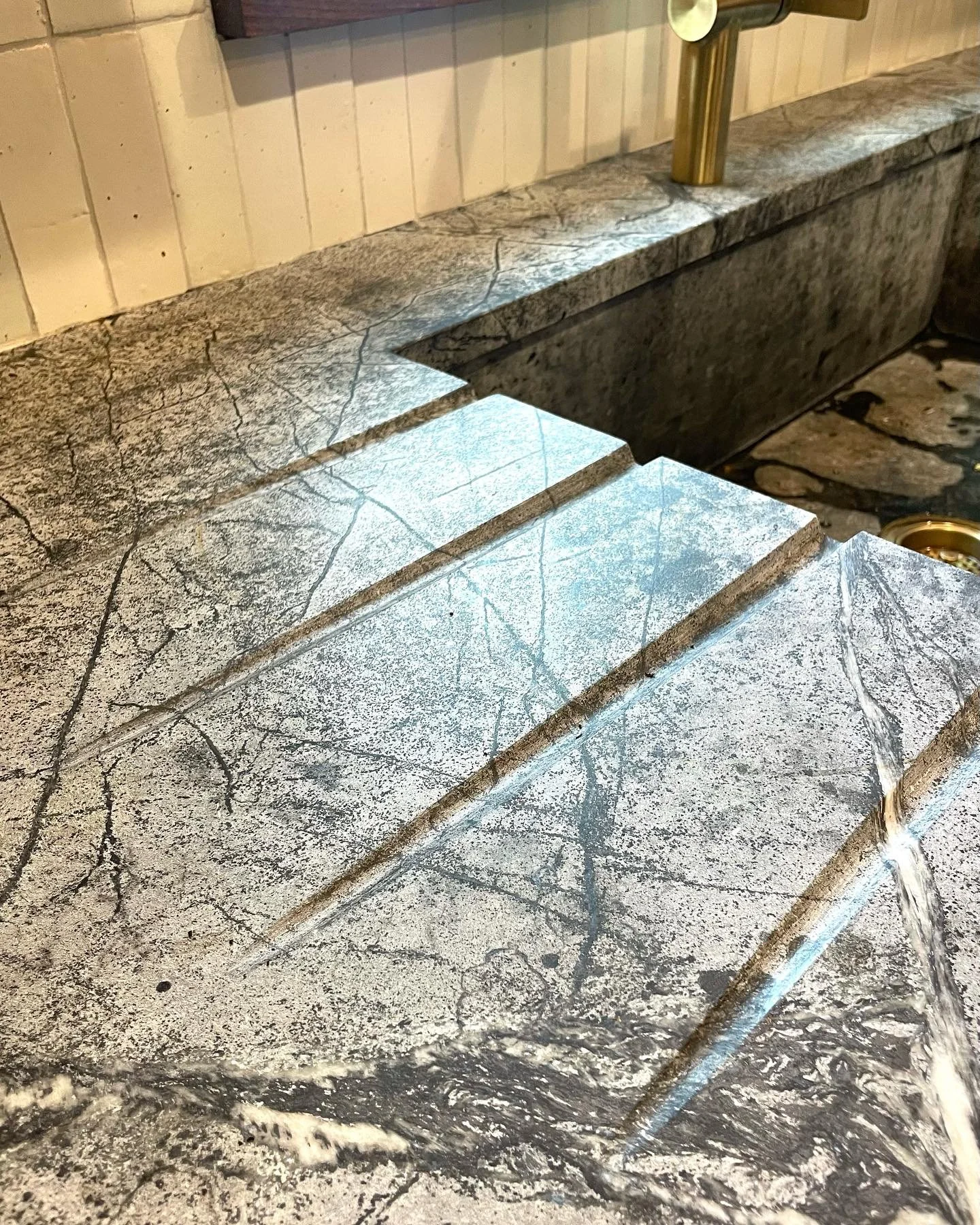 Close-up of a marble or granite countertop with a waterfall edge, featuring grey and white veining, with water running down the surface. Heartwood Renovations. West Hartford, CT