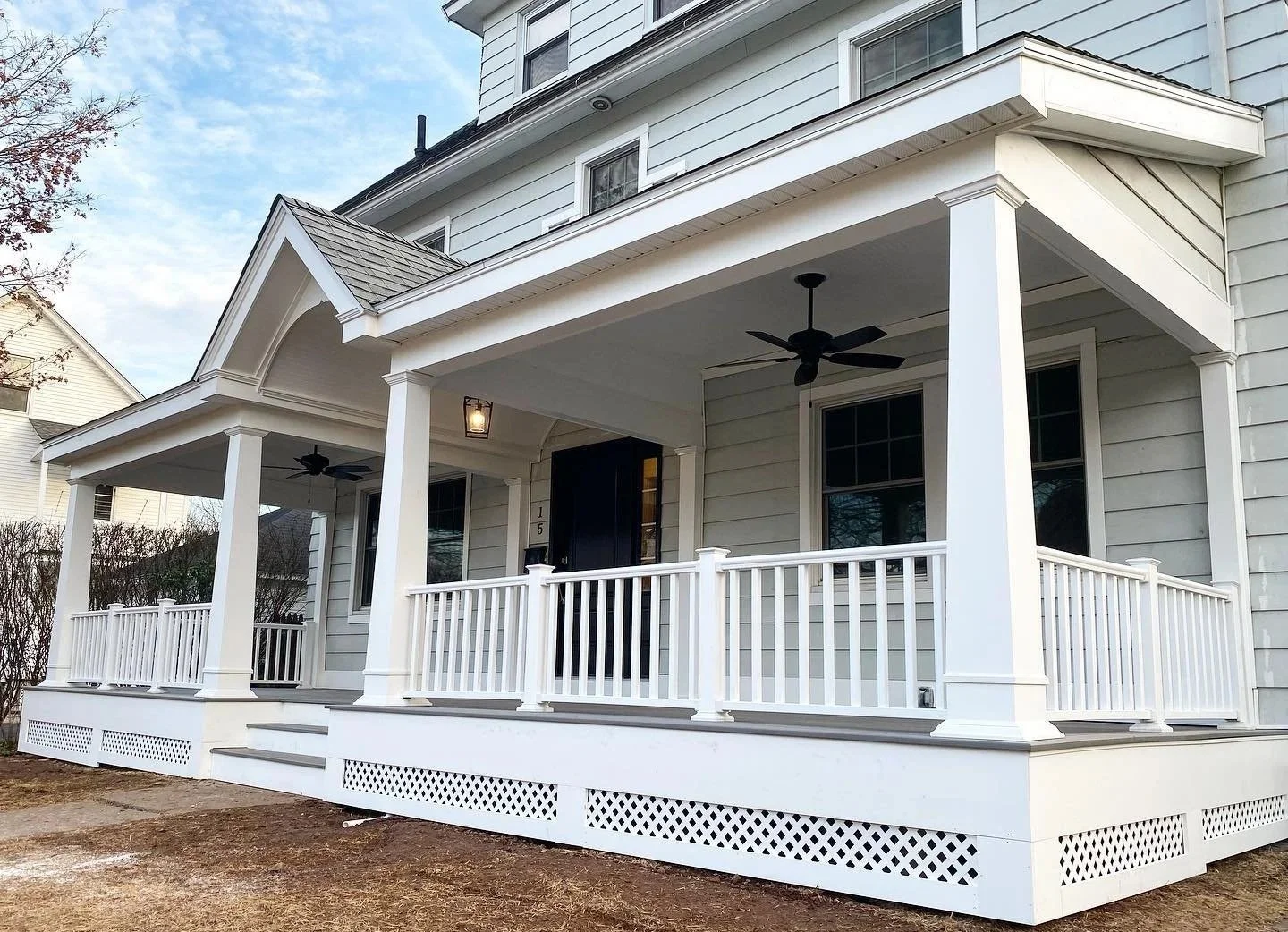 Front view of a white two-story house with a covered porch, white railing, black front door, and black ceiling fans, with a partly cloudy sky overhead. Heartwood Renovations. West Hartford, CT