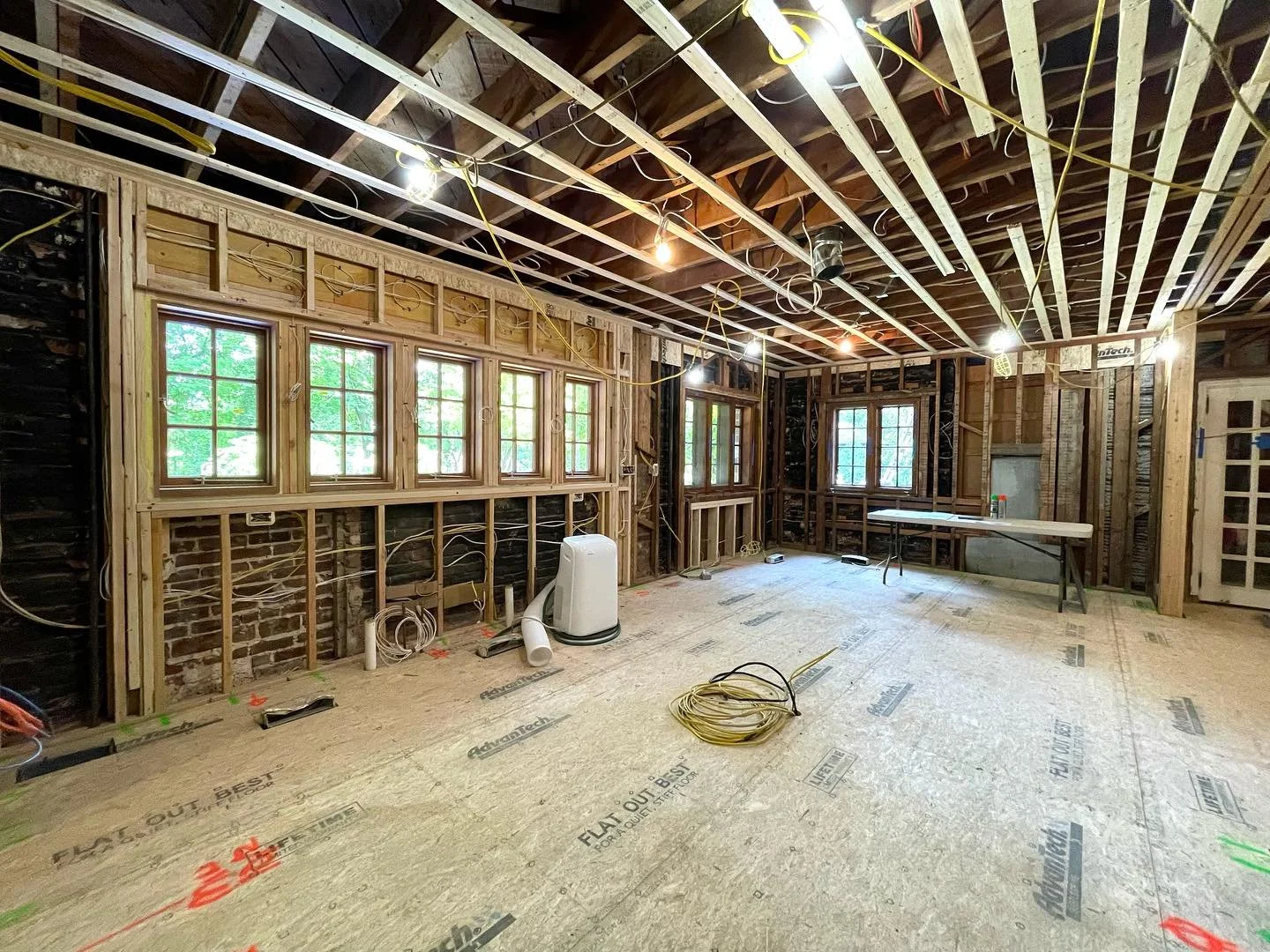 Interior of a room under construction with exposed wooden framing, multiple windows, ceiling wiring, and construction materials on the floor. Heartwood Renovations. West Hartford, CT